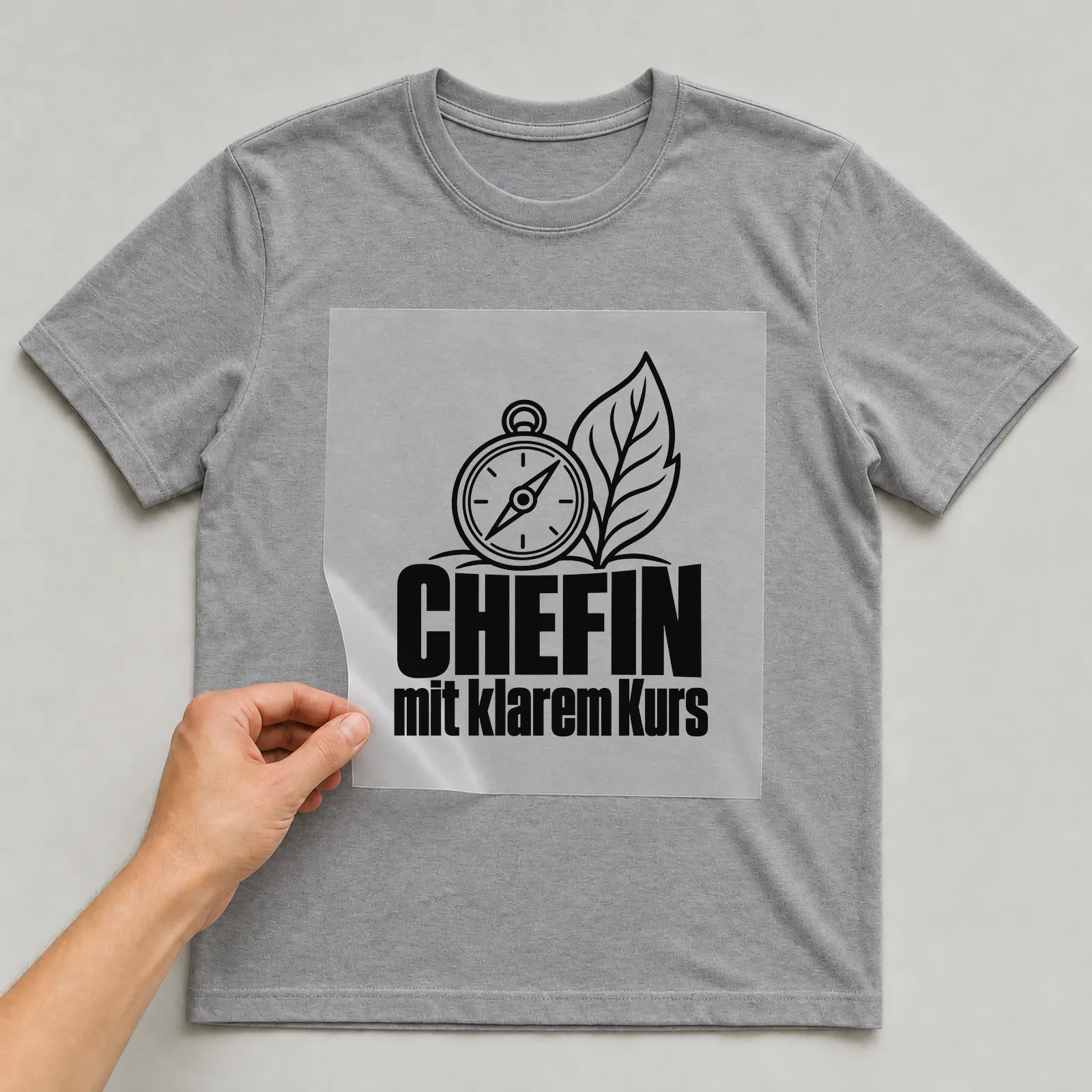 Bügelbild „Chefin mit klarem Kurs“ auf grauem T-Shirt, Folie wird aufgelegt