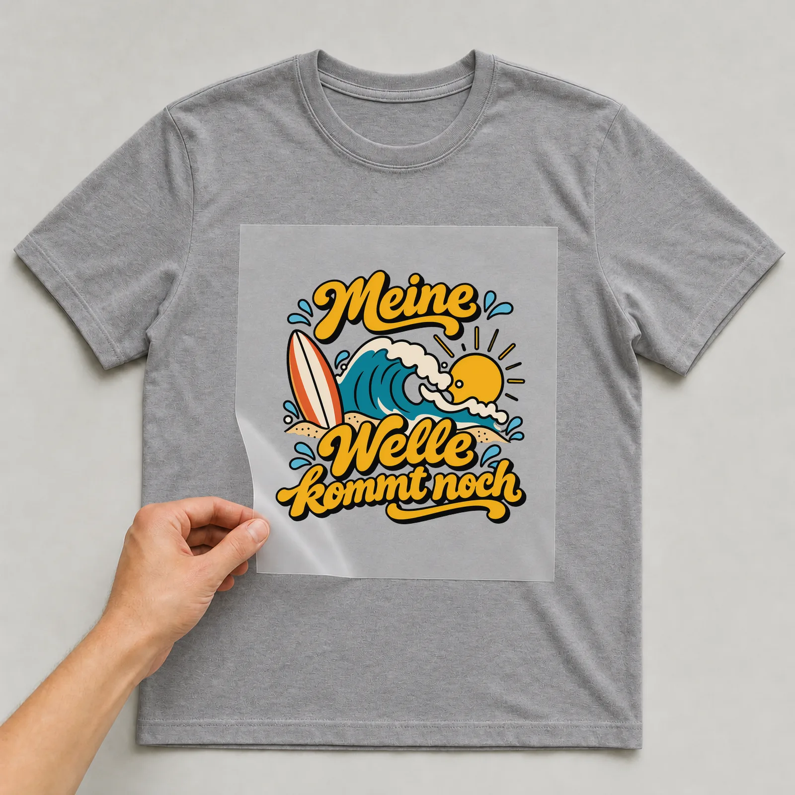 Bügelbild „Meine Welle kommt noch“ auf grauem T-Shirt, Folie wird aufgelegt