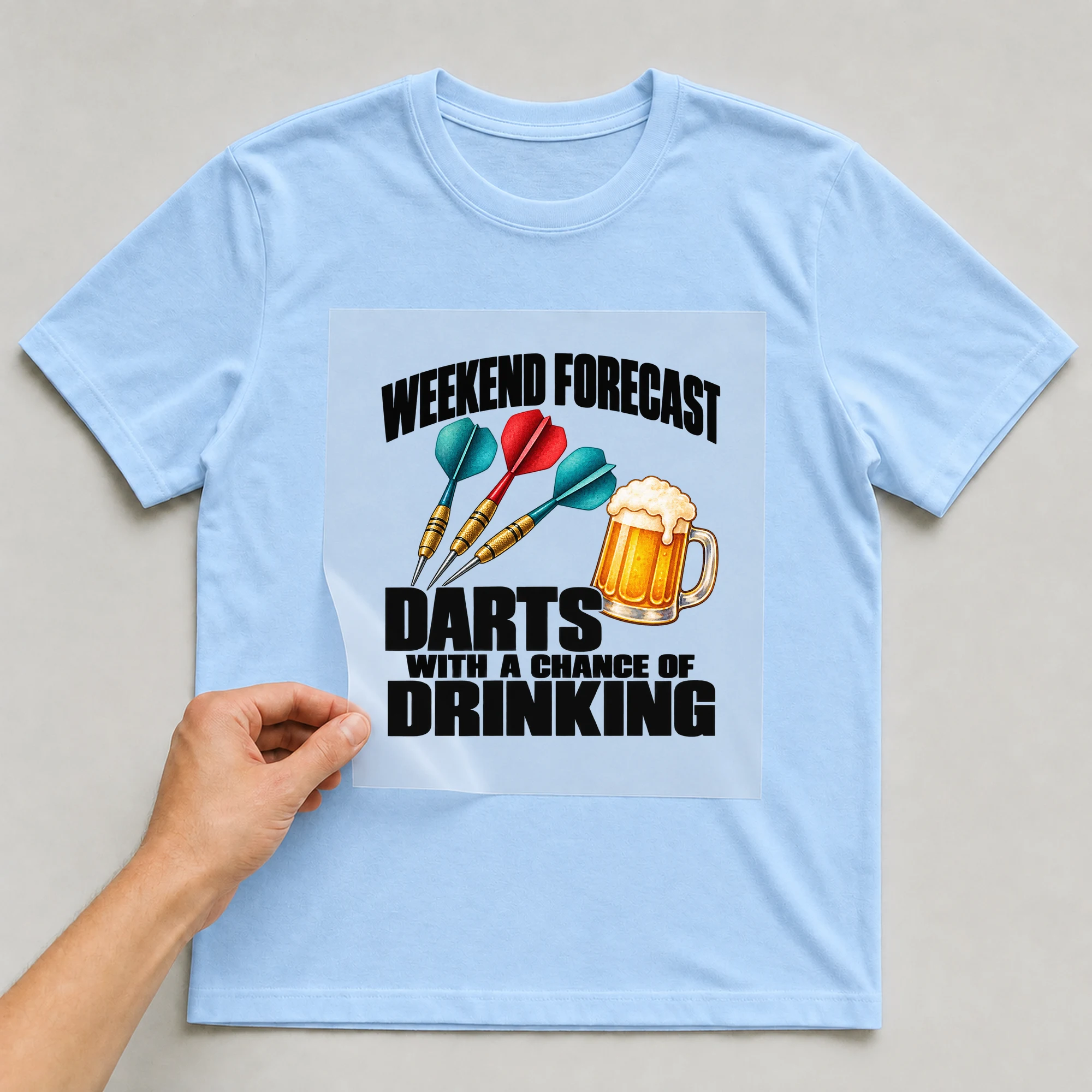 Bügelbild „Weekend Forecast Darts With A Chance Of Drinking“ auf babyblauem T-Shirt, Folie wird aufgelegt