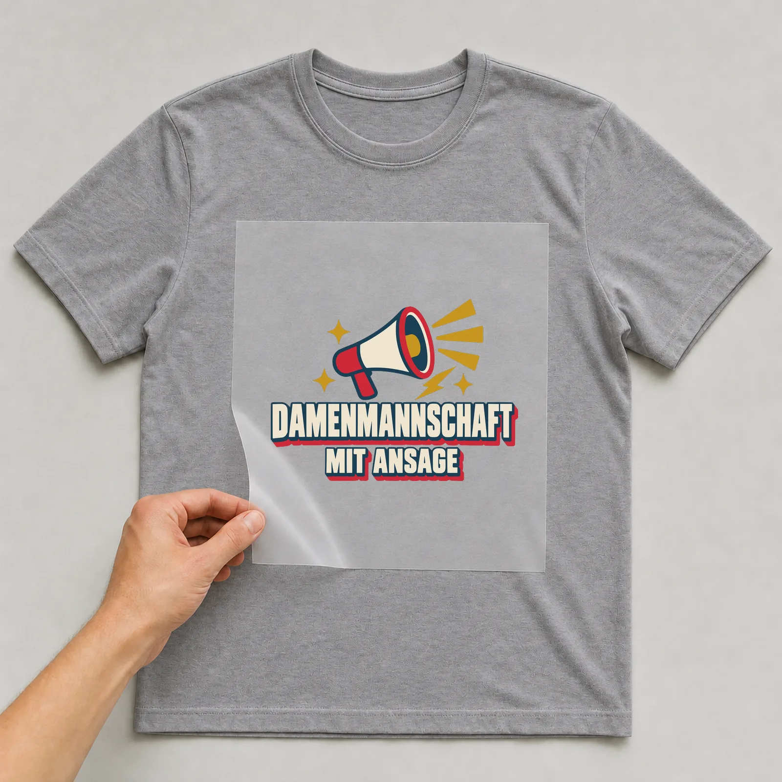 Bügelbild Damenmannschaft mit Ansage auf grauem T-Shirt, Folie wird aufgelegt