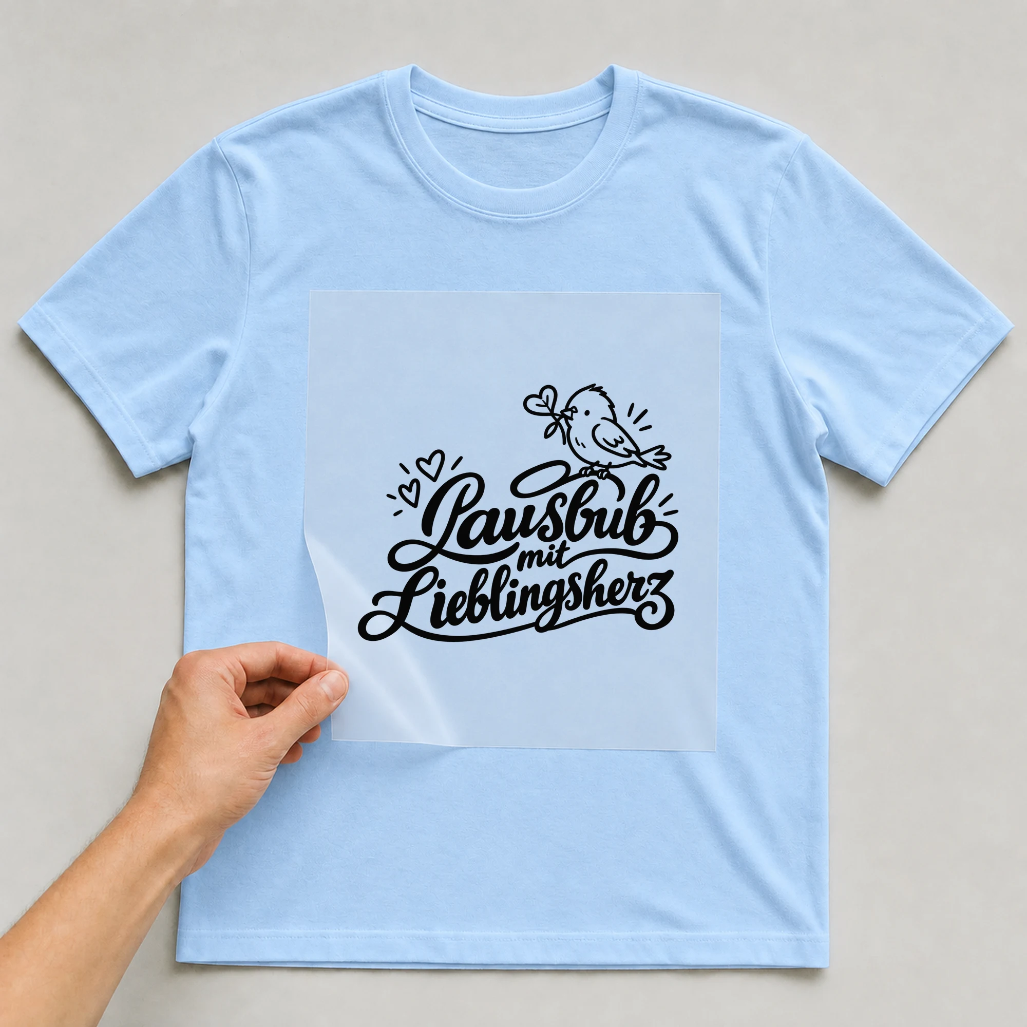 Bügelbild „Lausbub mit Lieblingsherz“ auf babyblauem T-Shirt, Folie wird aufgelegt