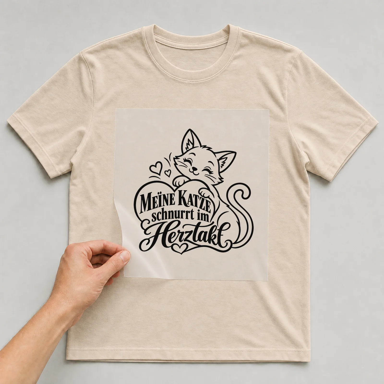 Bügelbild „Meine Katze schnurrt im Herztakt“ auf beigem T-Shirt, Folie wird aufgelegt
