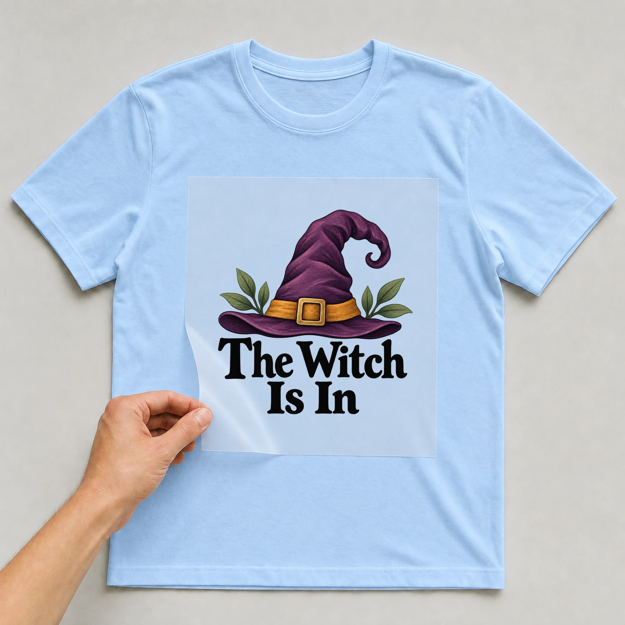 Bügelbild „The Witch Is In“ auf babyblauem T-Shirt, Folie wird aufgelegt
