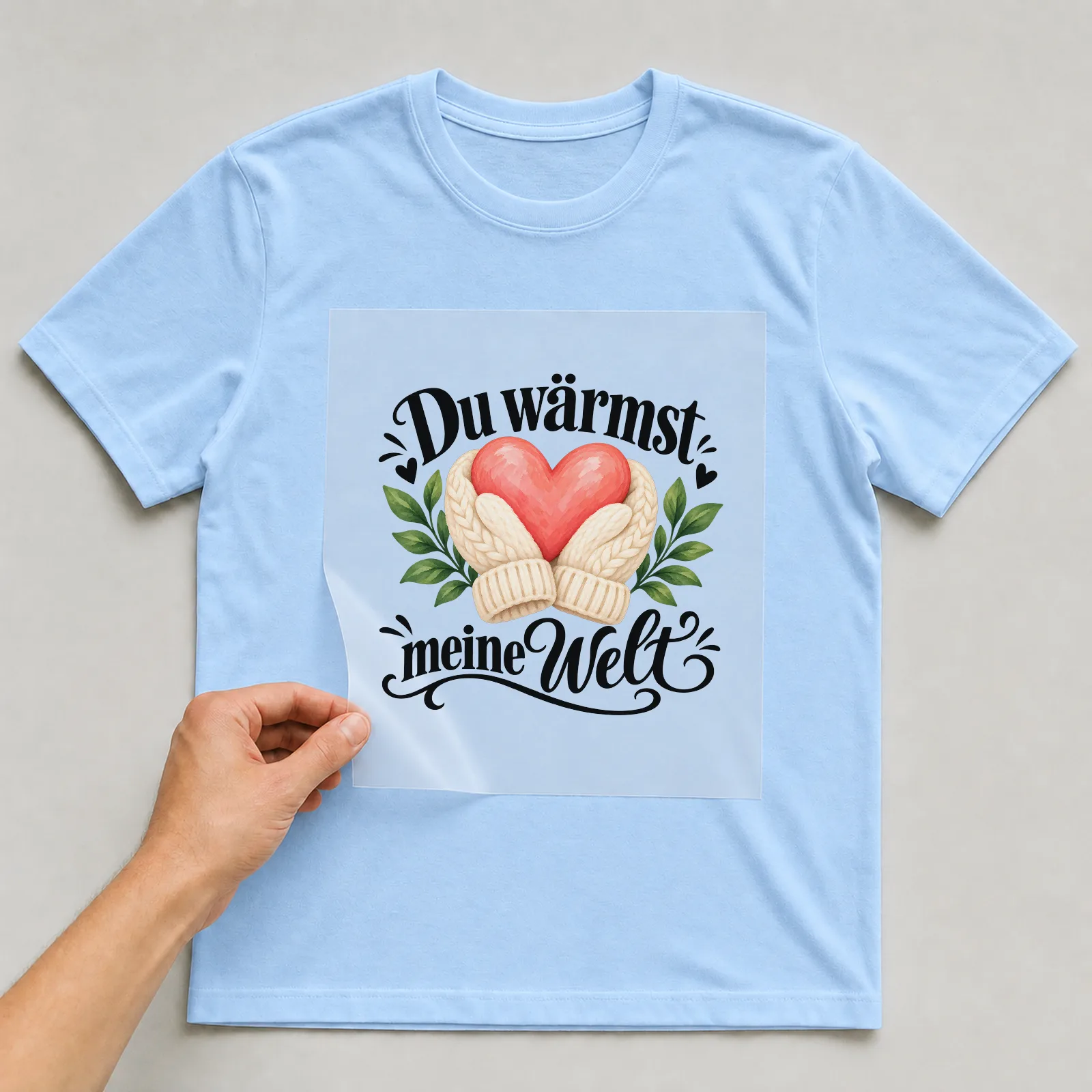Bügelbild „Du wärmst meine Welt“ auf hellblauem T-Shirt, Folie wird aufgelegt