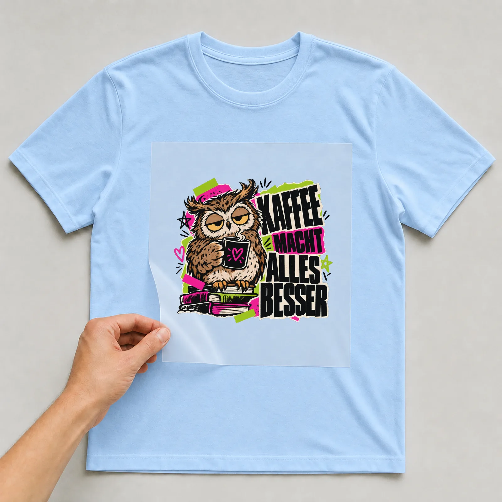 Bügelbild „Kaffee macht alles besser“ auf hellblauem T-Shirt, Folie wird aufgelegt