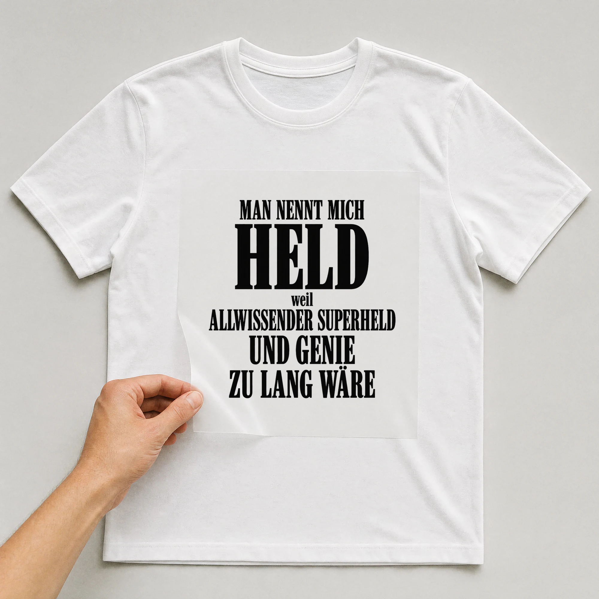 Bügelbild „Man nennt mich Held, weil Allwissender Superheld und Genie zu lang wäre“ auf weißem T-Shirt, Folie wird aufgelegt
