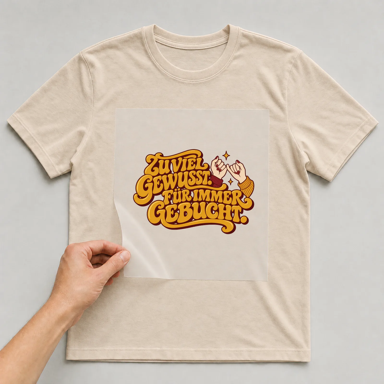 Bügelbild „Zu viel gewusst. Für immer gebucht.“ auf beigem T-Shirt, Folie wird aufgelegt