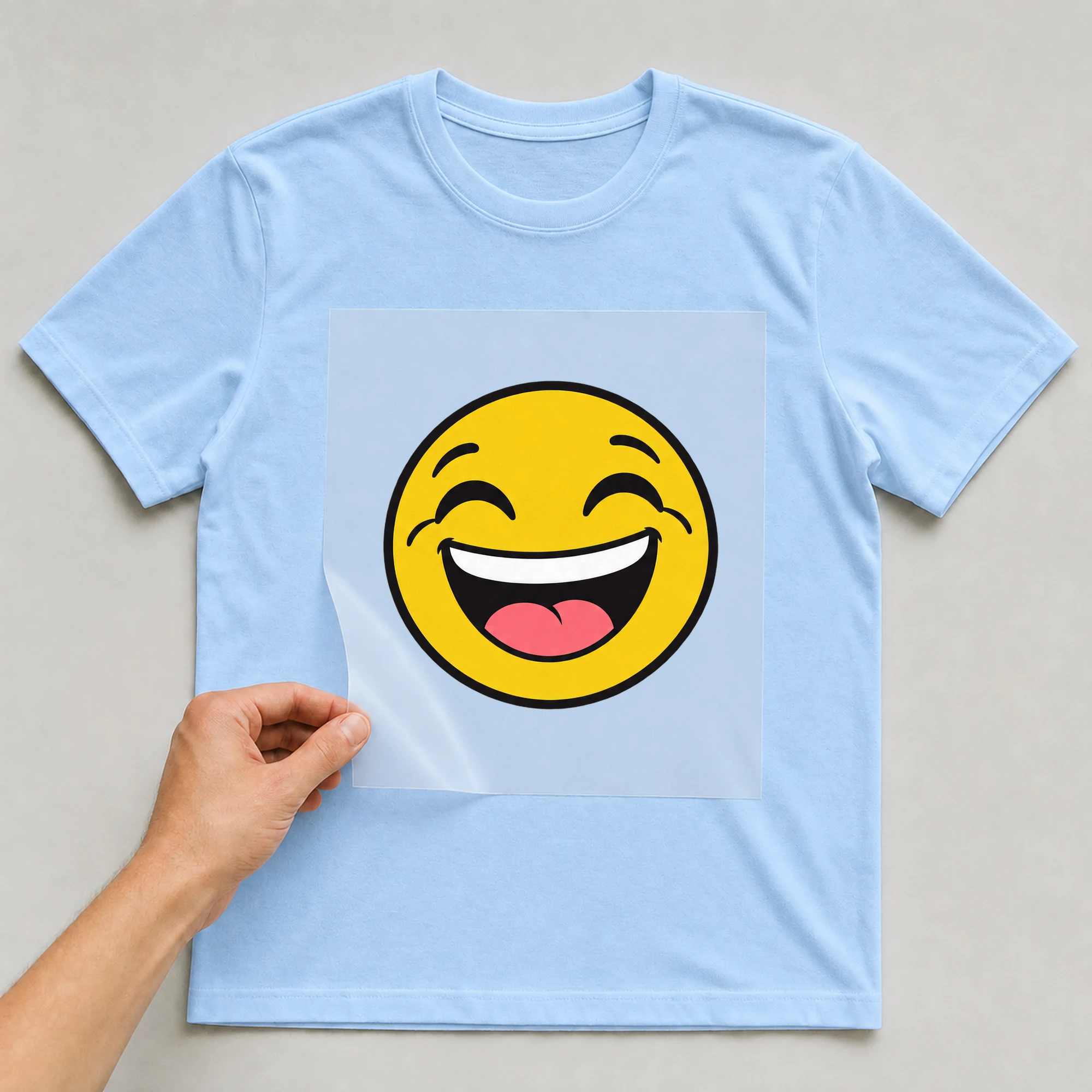 Bügelbild „Lachendes gelbes Gesicht“ auf babyblauem T-Shirt, Folie wird aufgelegt
