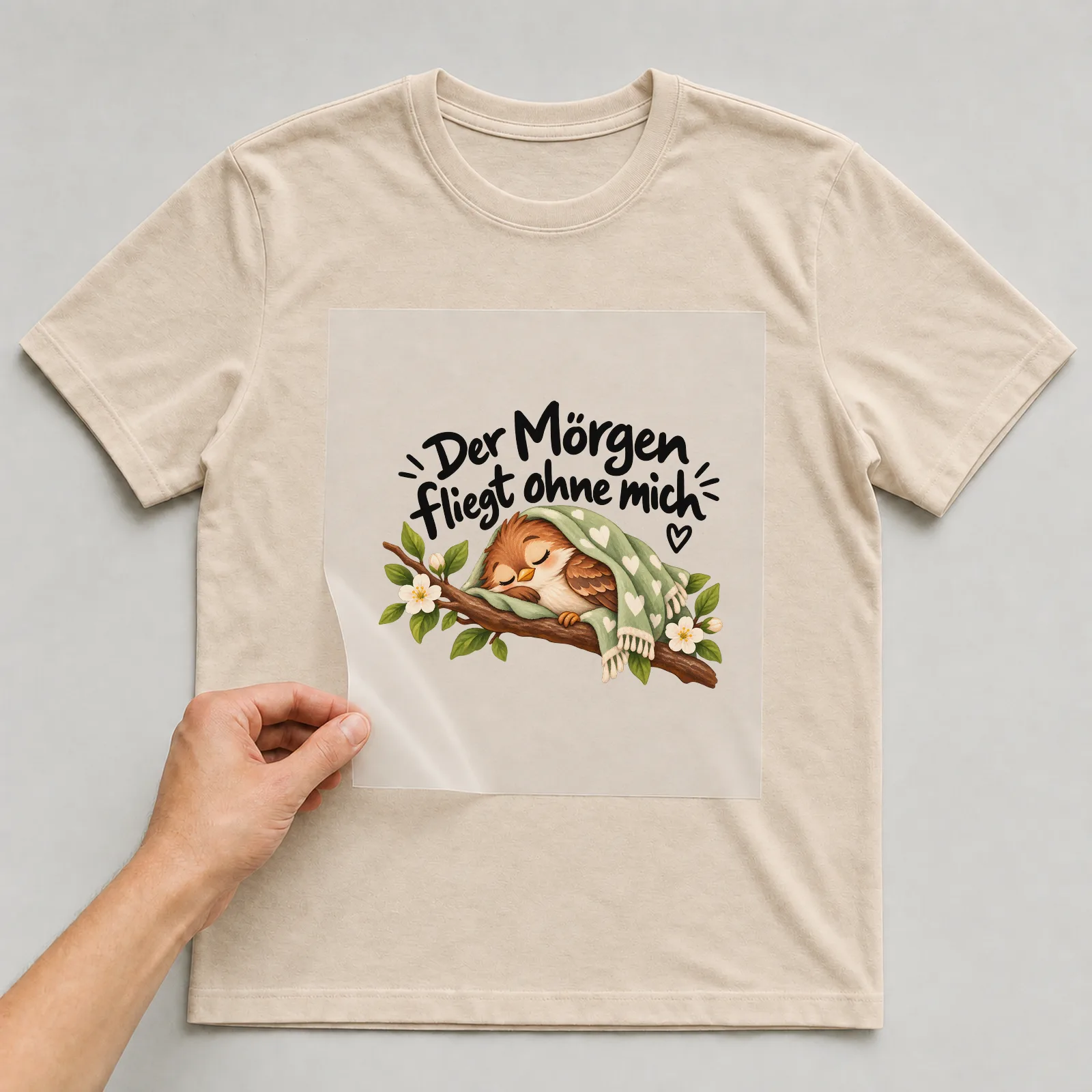 Bügelbild „Der Morgen fliegt ohne mich“ auf beigem T-Shirt, Folie wird aufgelegt