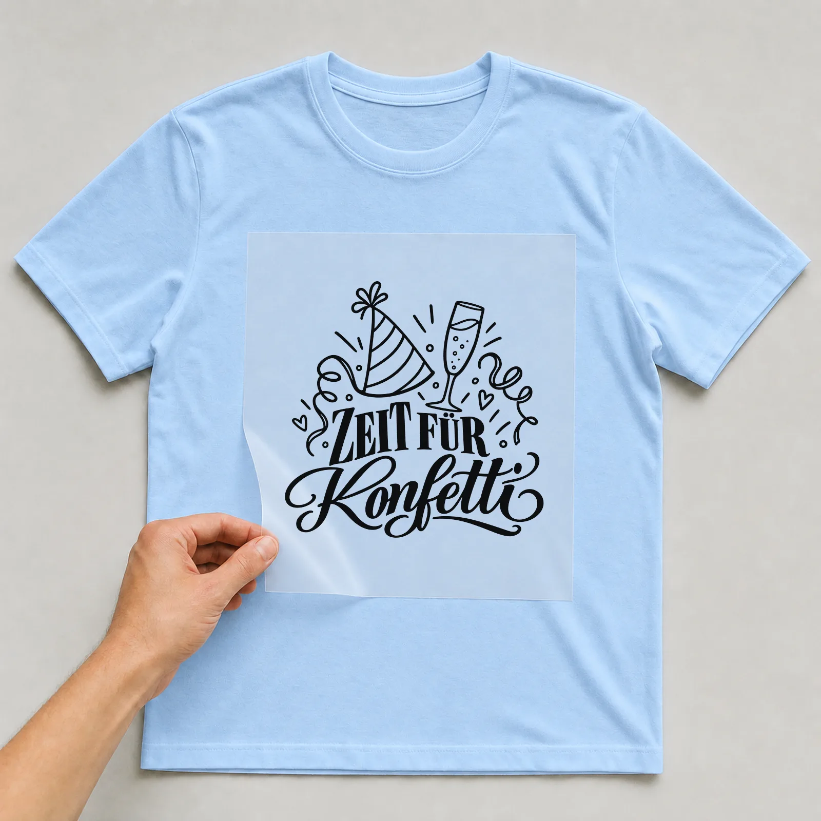 Bügelbild „Zeit für Konfetti“ auf hellblauem T-Shirt, Folie wird aufgelegt