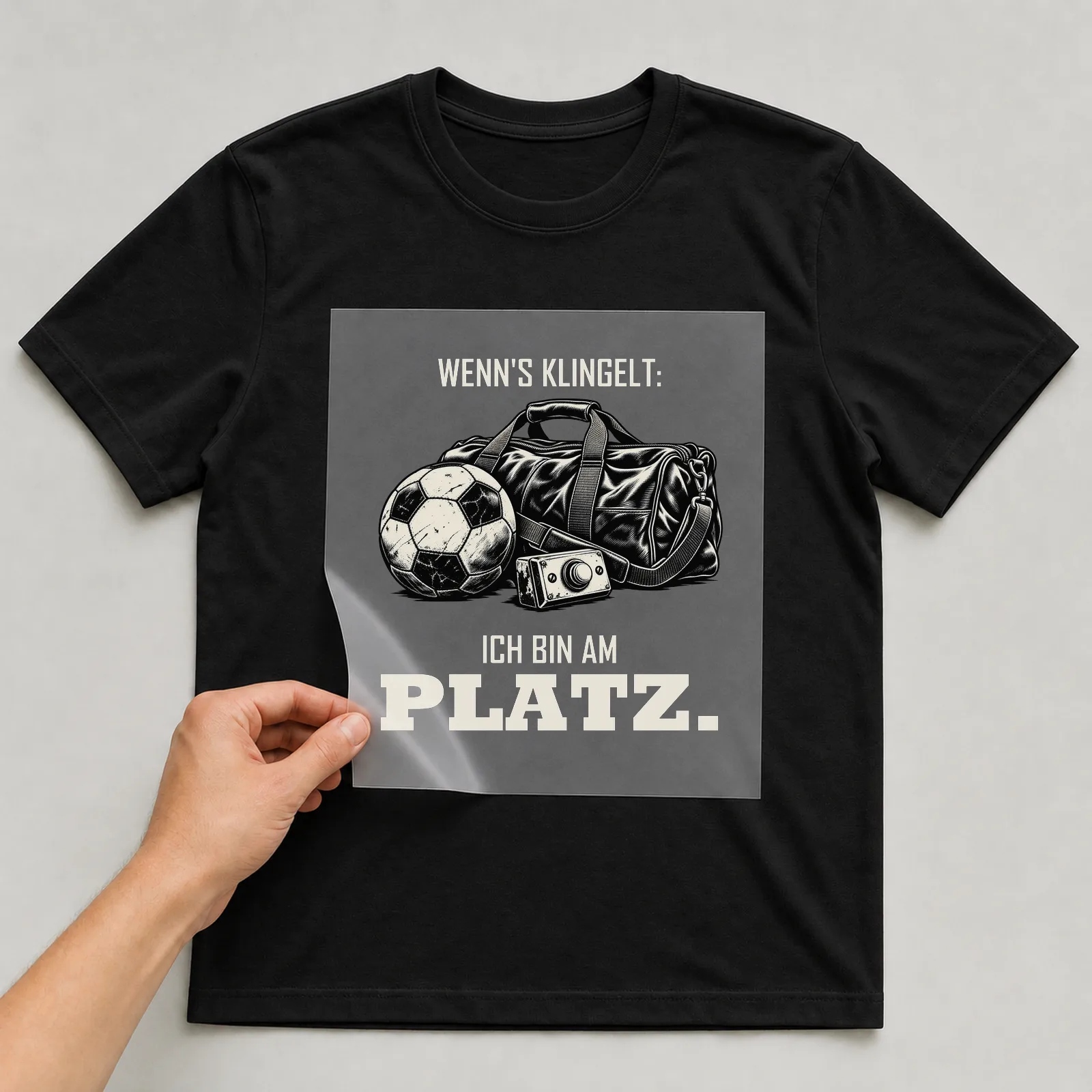 Bügelbild „Wenn's klingelt: ich bin am Platz“ auf schwarzem T-Shirt, Folie wird aufgelegt