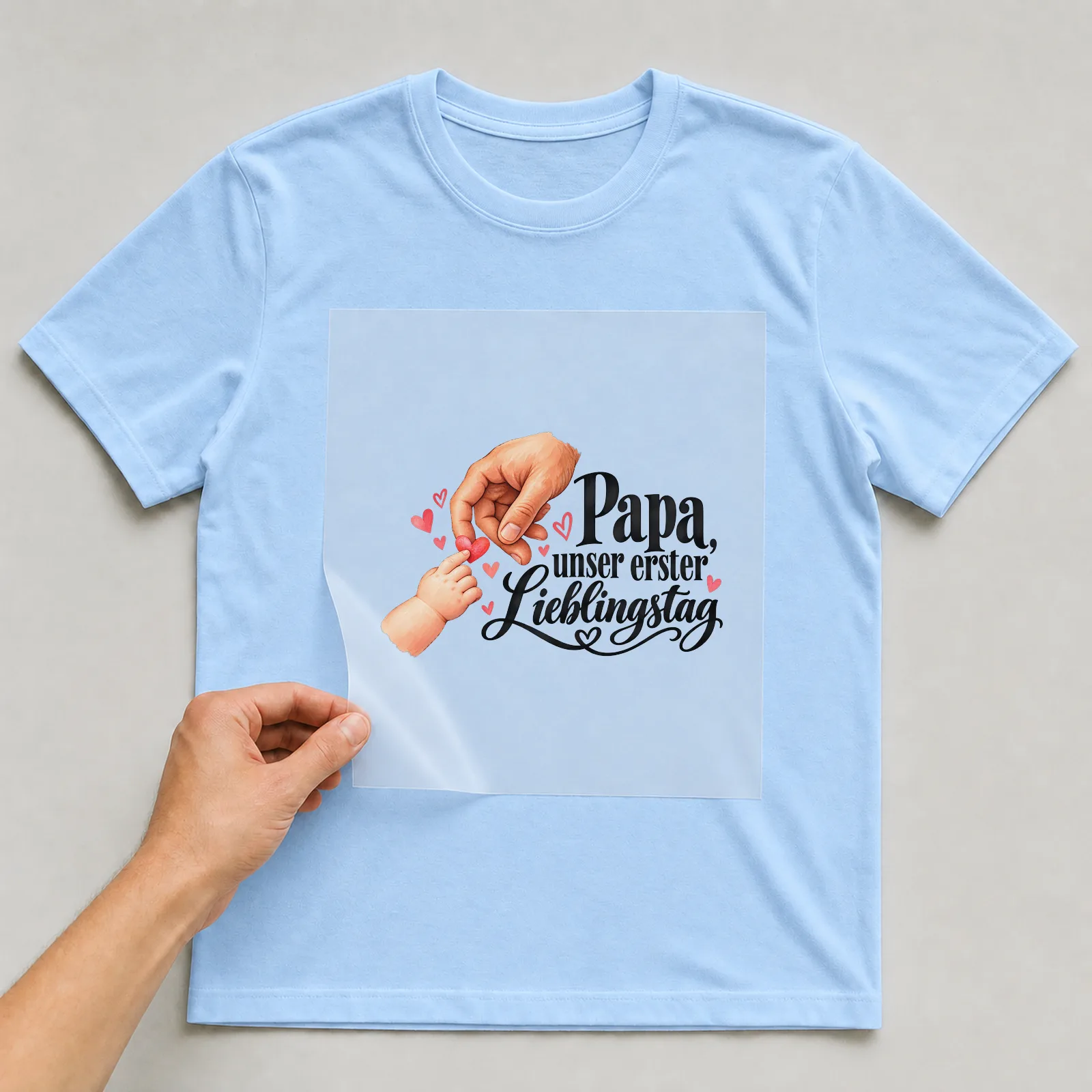 Bügelbild „Papa, unser erster Lieblingstag“ auf hellblauem T-Shirt, Folie wird aufgelegt