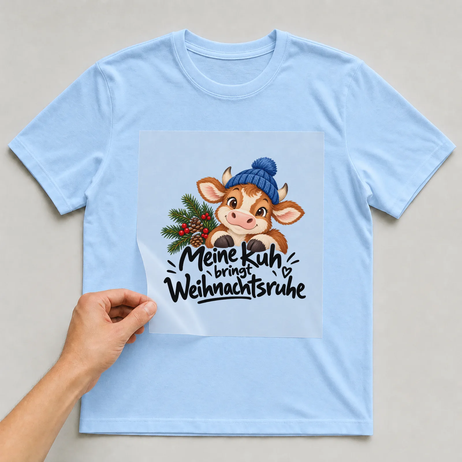 Bügelbild „Meine Kuh bringt Weihnachtsruhe“ auf hellblauem T-Shirt, Folie wird aufgelegt