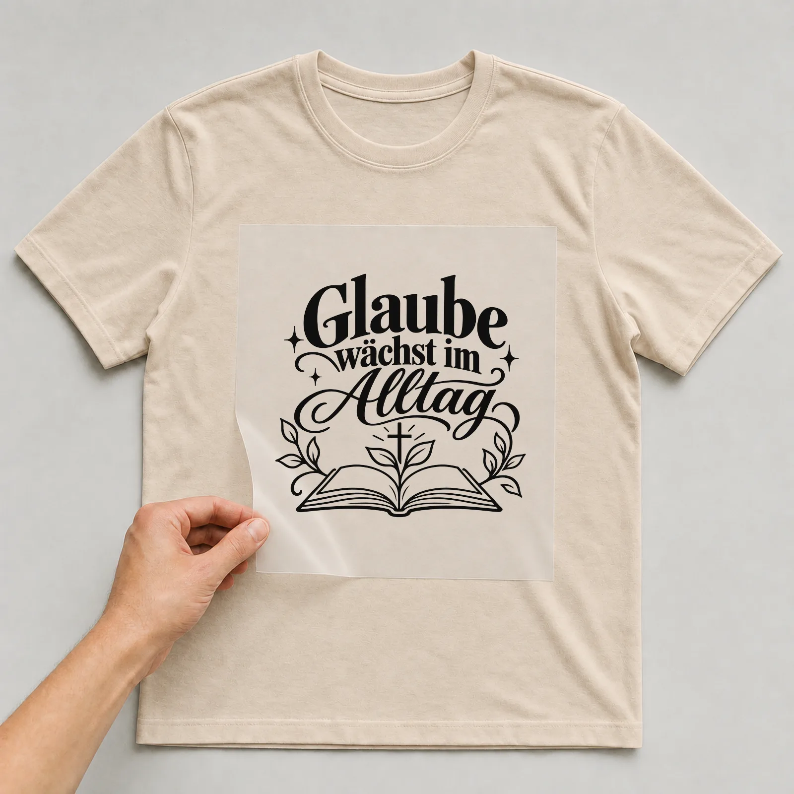 Bügelbild „Glaube wächst im Alltag“ auf beigem T-Shirt, Folie wird aufgelegt
