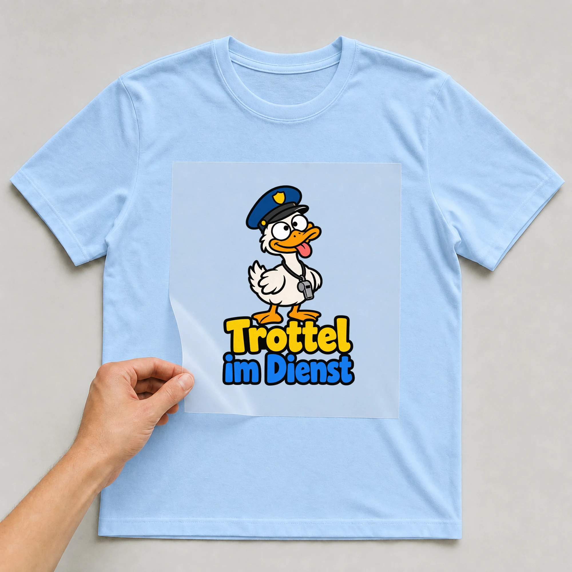 Bügelbild „Trottel im Dienst“ auf babyblauem T-Shirt, Folie wird aufgelegt