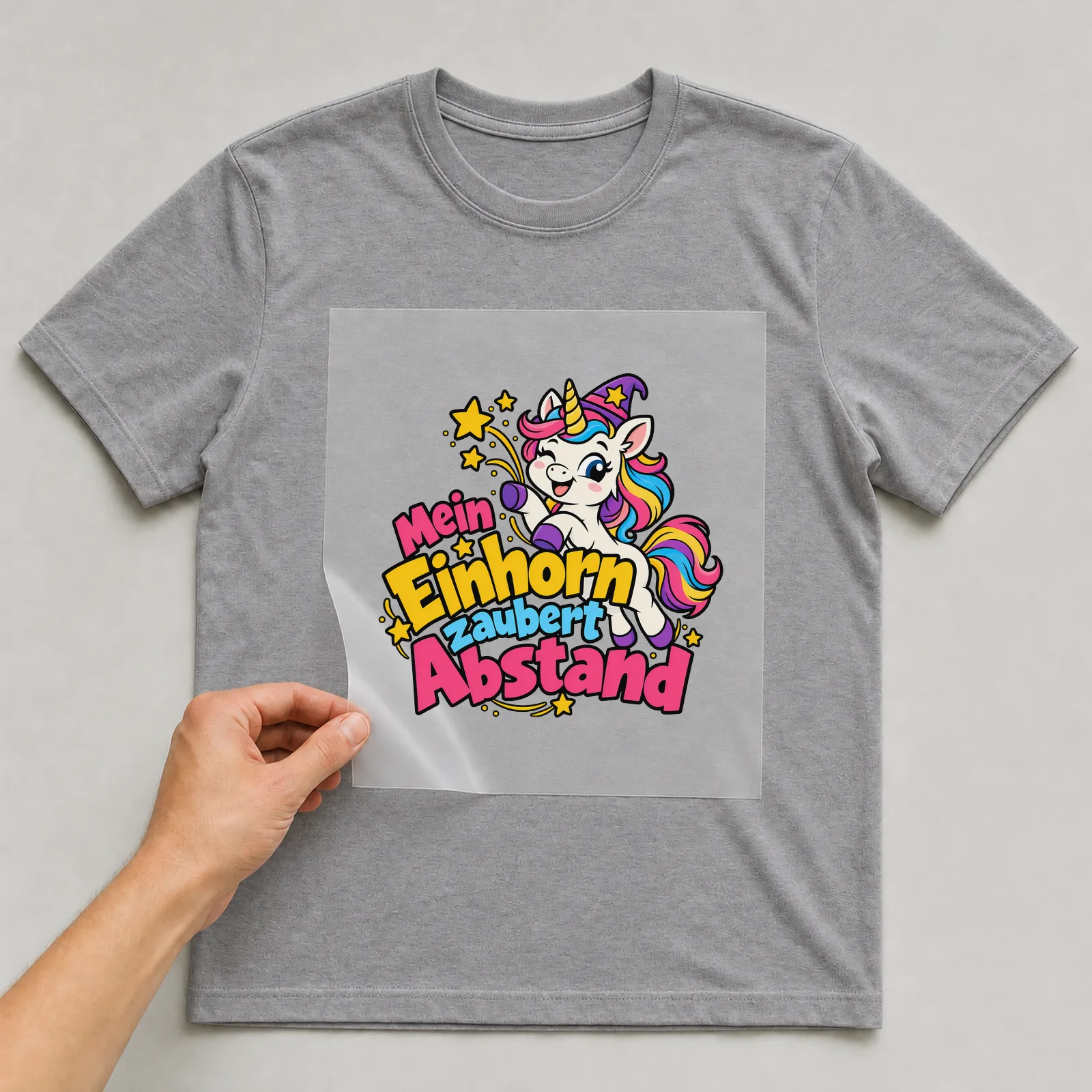 Bügelbild „Mein Einhorn zaubert Abstand“ auf grauem T-Shirt, Folie wird aufgelegt