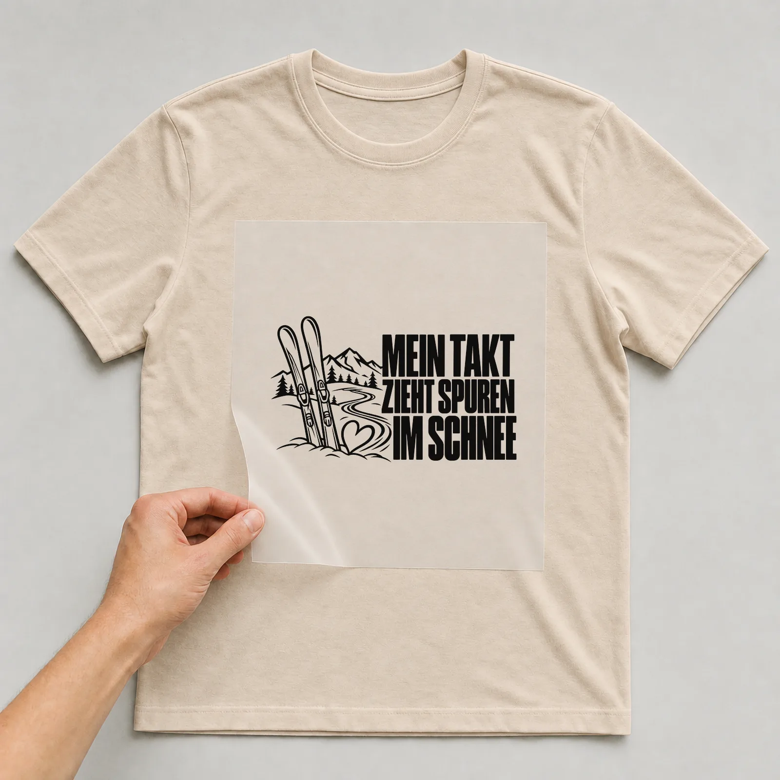 Bügelbild „Mein Takt zieht spuren im Schnee“ auf beigem T-Shirt, Folie wird aufgelegt