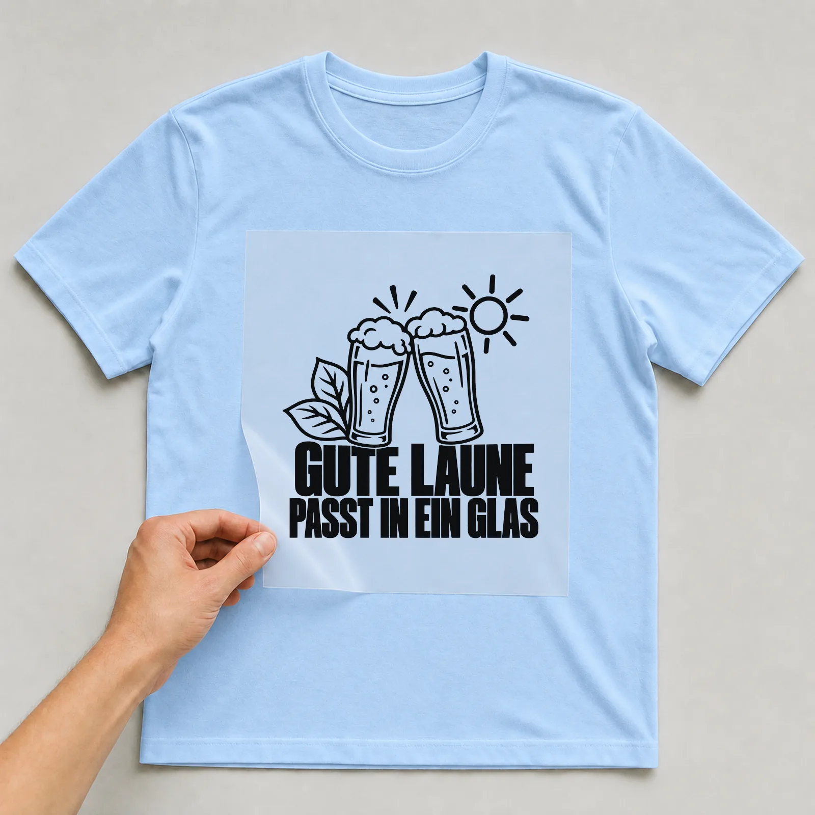 Bügelbild „Gute Laune passt in ein Glas“ auf hellblauem T-Shirt, Folie wird aufgelegt