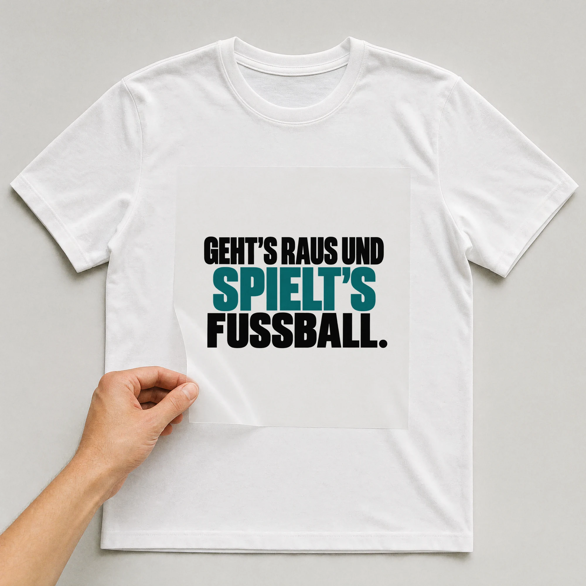 Bügelbild „Geht's raus und spielt's Fußball.“ auf weißem T-Shirt, Folie wird aufgelegt