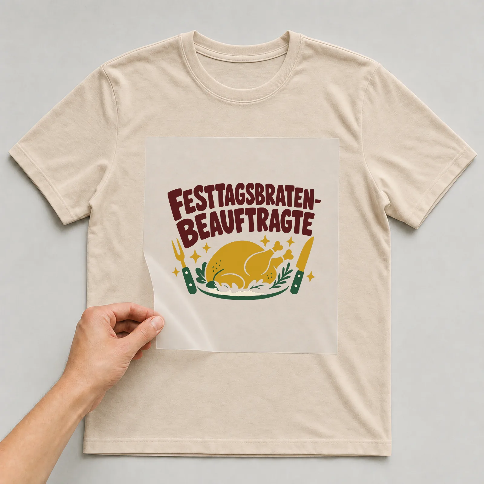 Bügelbild Festtagsbraten-Beauftragte auf beigem T-Shirt, Folie wird aufgelegt