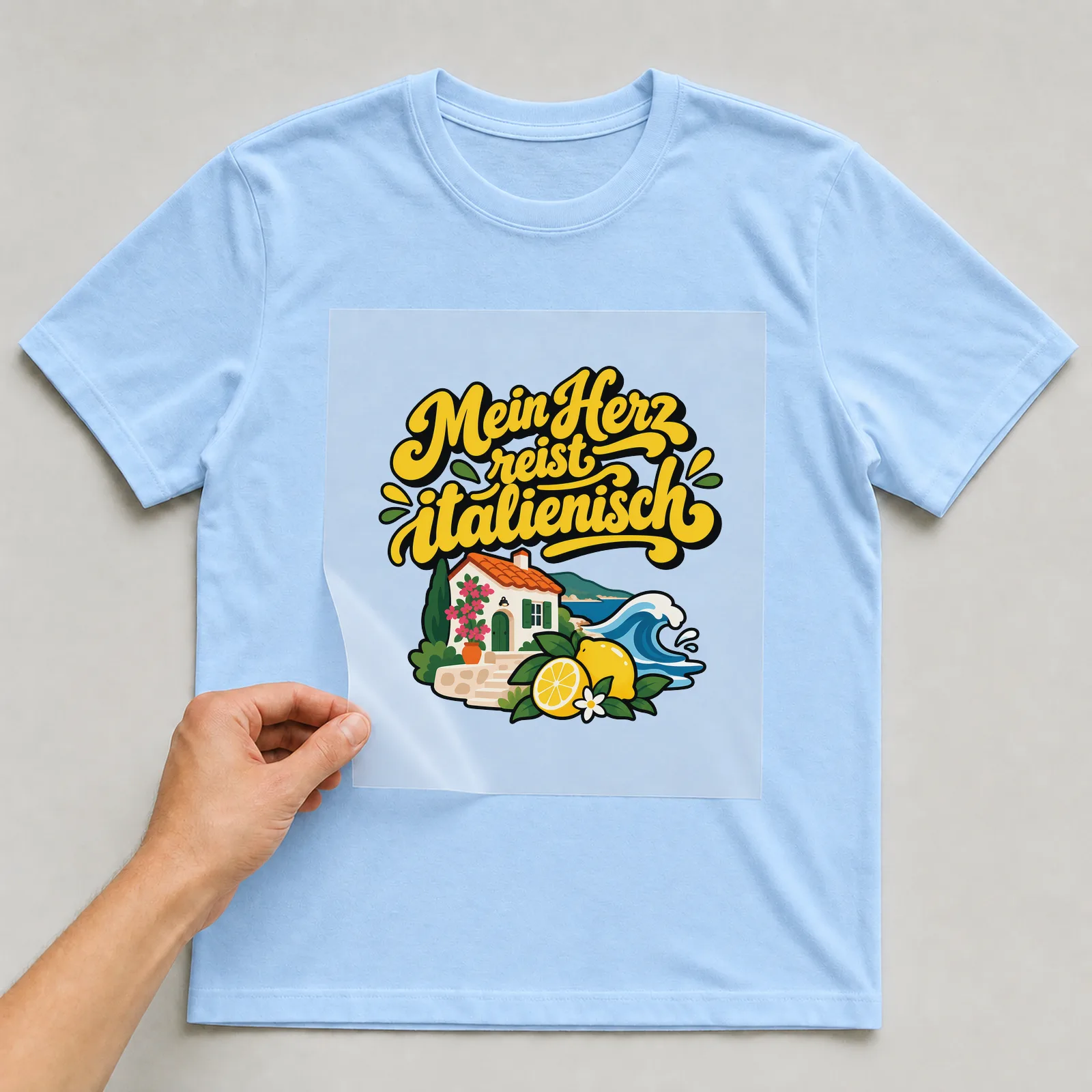 Bügelbild „Mein Herz reist italienisch“ auf hellblauem T-Shirt, Folie wird aufgelegt