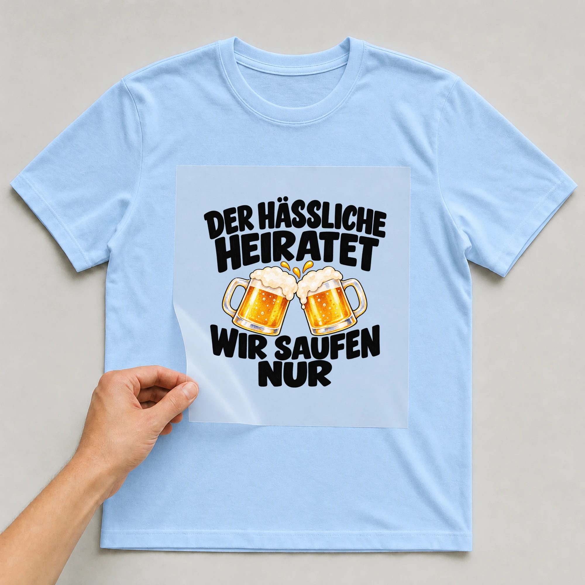 Bügelbild „Der hässliche heiratet wir saufen nur“ auf babyblauem T-Shirt, Folie wird aufgelegt