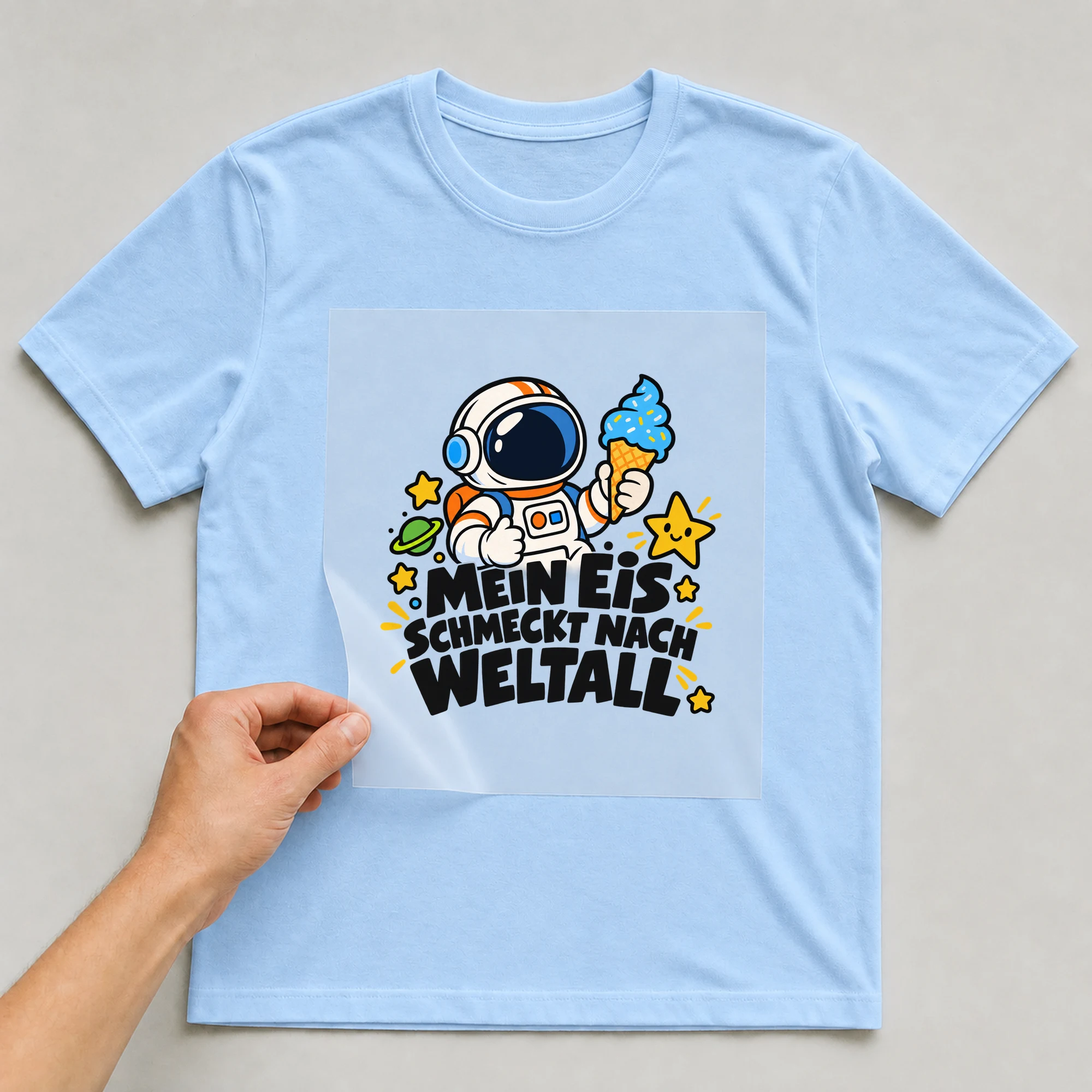 Bügelbild „Mein Eis schmeckt nach Weltall“ auf hellblauem T-Shirt, Folie wird aufgelegt