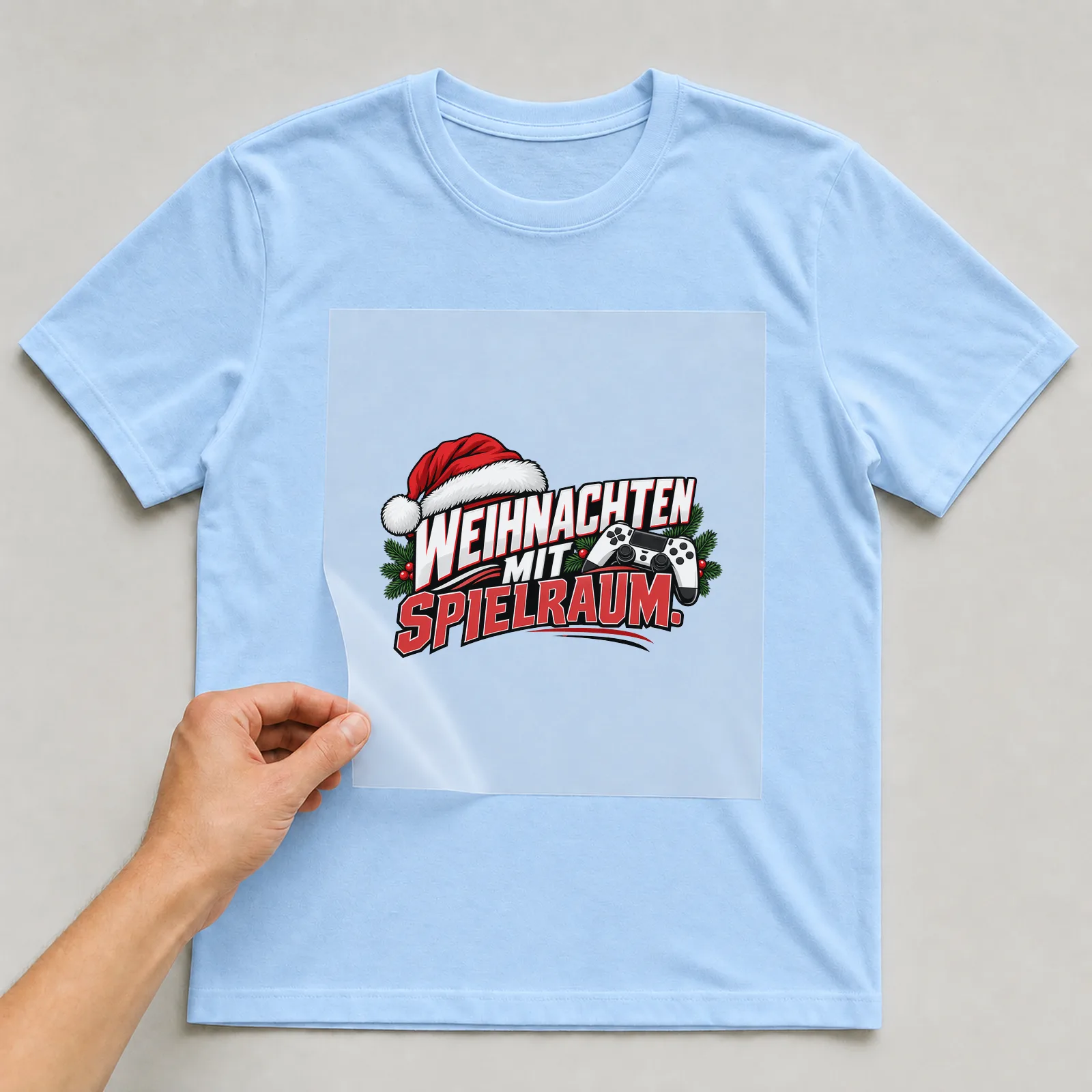 Bügelbild „Weihnachten mit Spielraum“ auf hellblauem T-Shirt, Folie wird aufgelegt