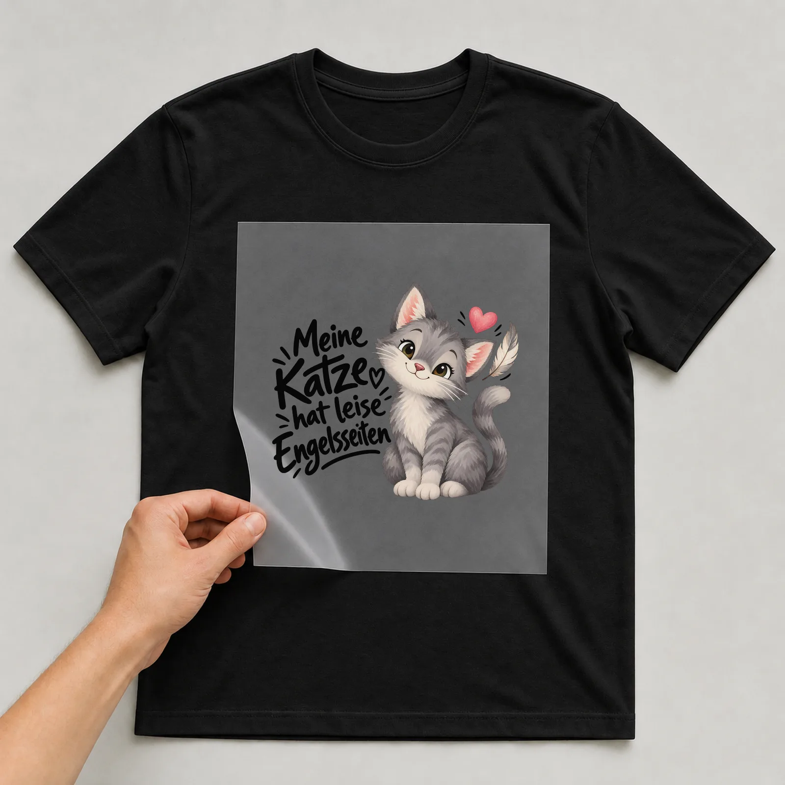 Bügelbild „Meine Katze hat leise Engelsseiten“ auf schwarzem T-Shirt, Folie wird aufgelegt
