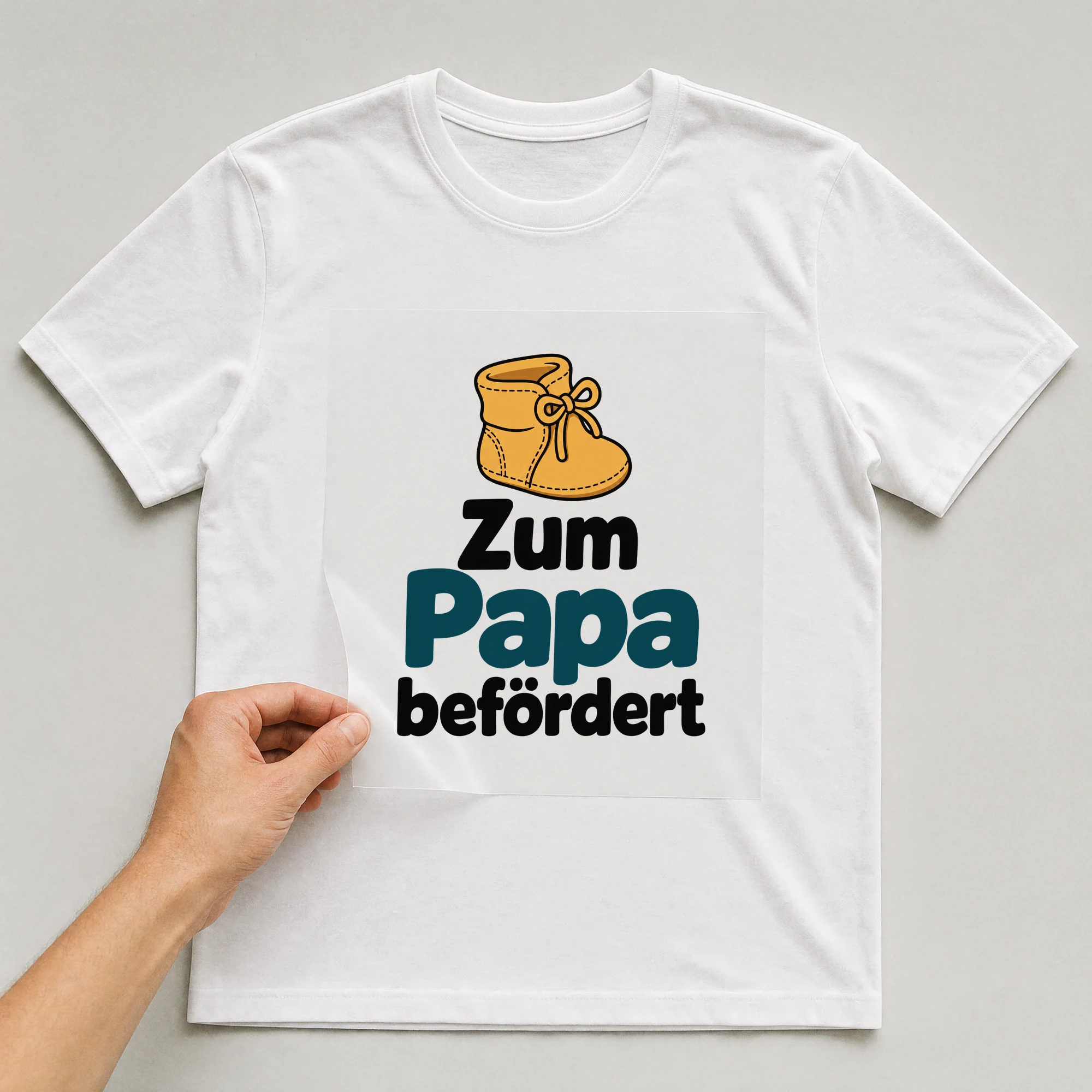 Bügelbild „Zum Papa befördert“ auf weißem T-Shirt, Folie wird aufgelegt