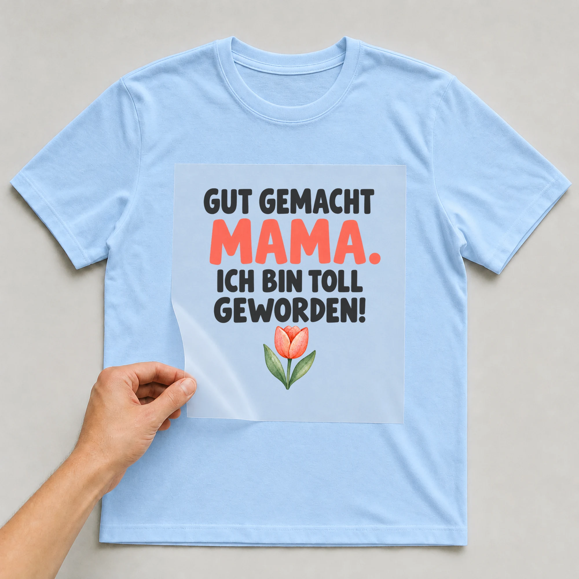 Bügelbild „Gut gemacht Mama. Ich bin toll geworden!“ auf babyblauem T-Shirt, Folie wird aufgelegt
