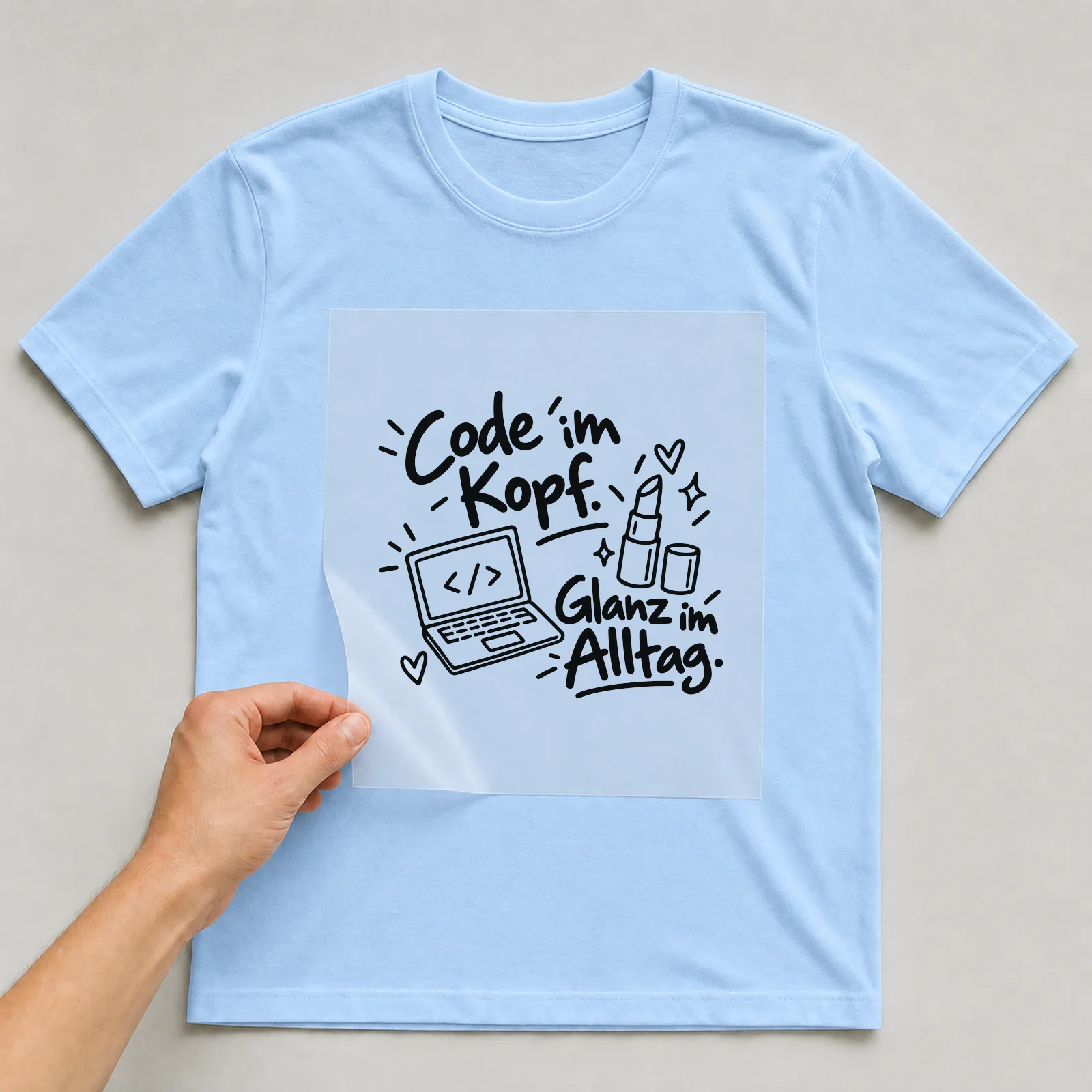 Bügelbild „Code im Kopf. Glanz im Alltag.“ auf hellblauem T-Shirt, Folie wird aufgelegt