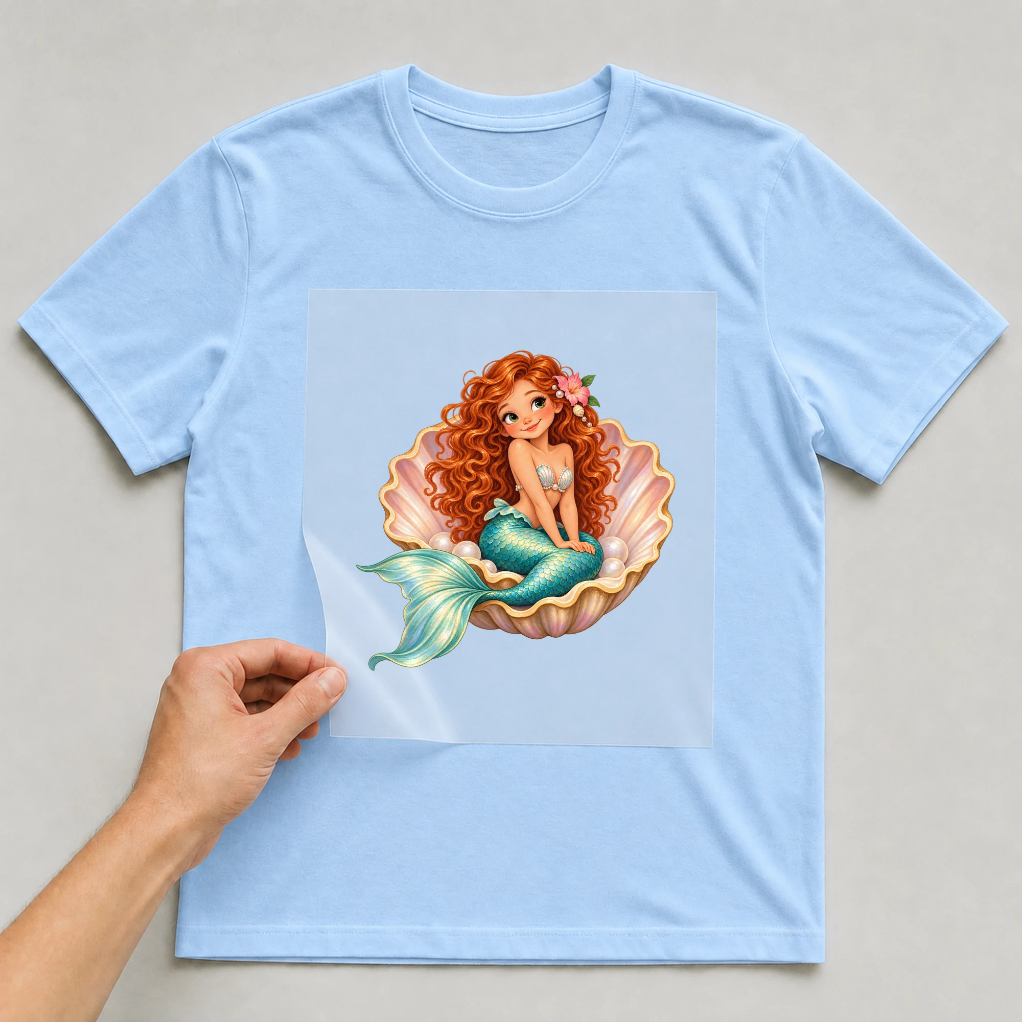 Bügelbild „Meerjungfrau mit Muschel“ auf babyblauem T-Shirt, Folie wird aufgelegt