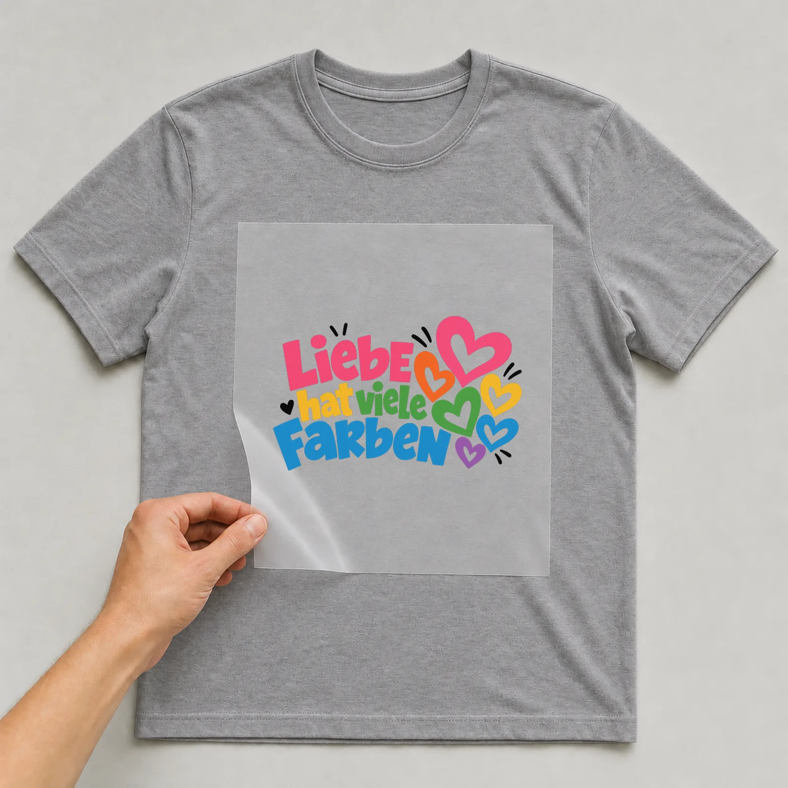 Bügelbild „Liebe hat viele Farben“ auf grauem T-Shirt, Folie wird aufgelegt