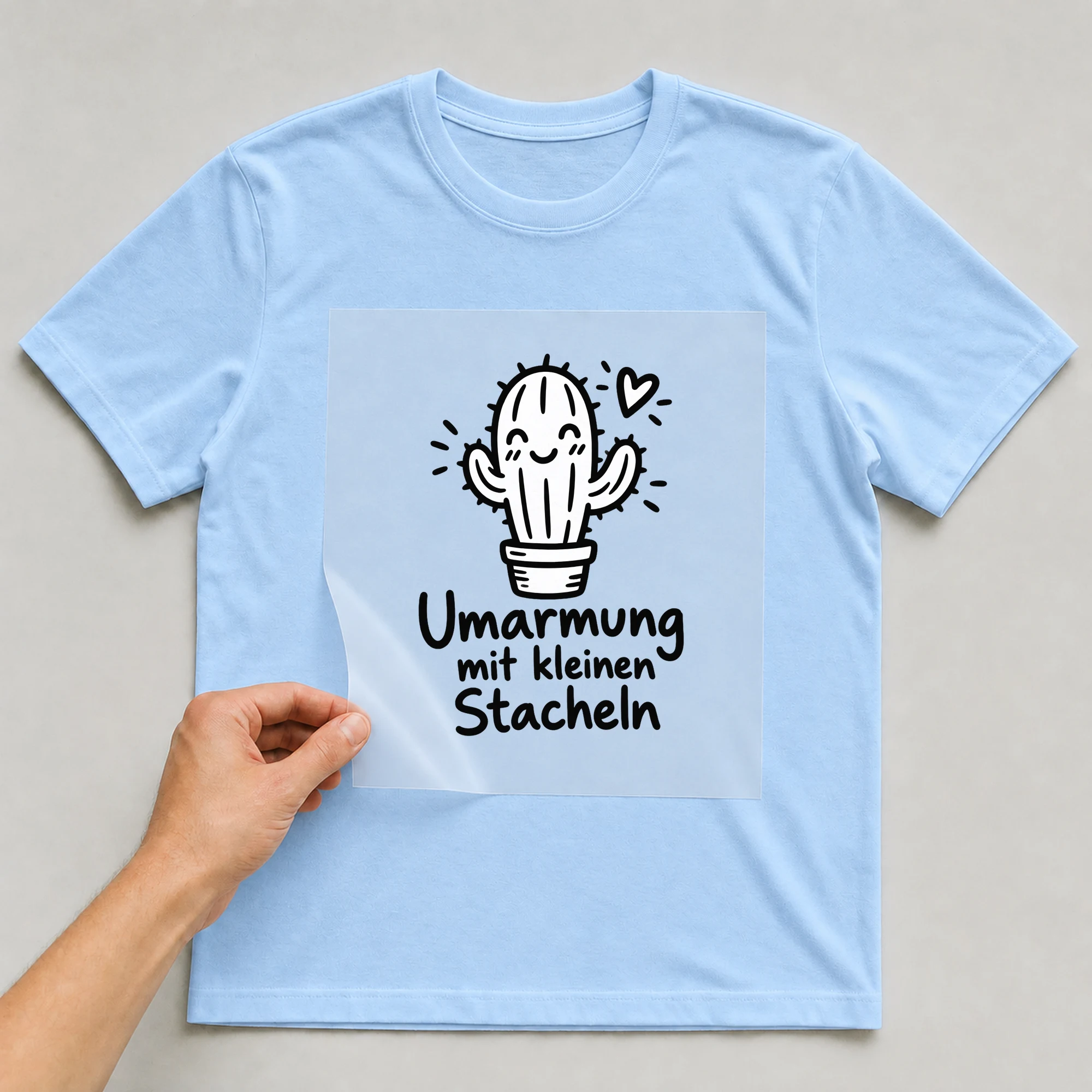 Bügelbild „Umarmung mit kleinen Stacheln“ auf hellblauem T-Shirt, Folie wird aufgelegt