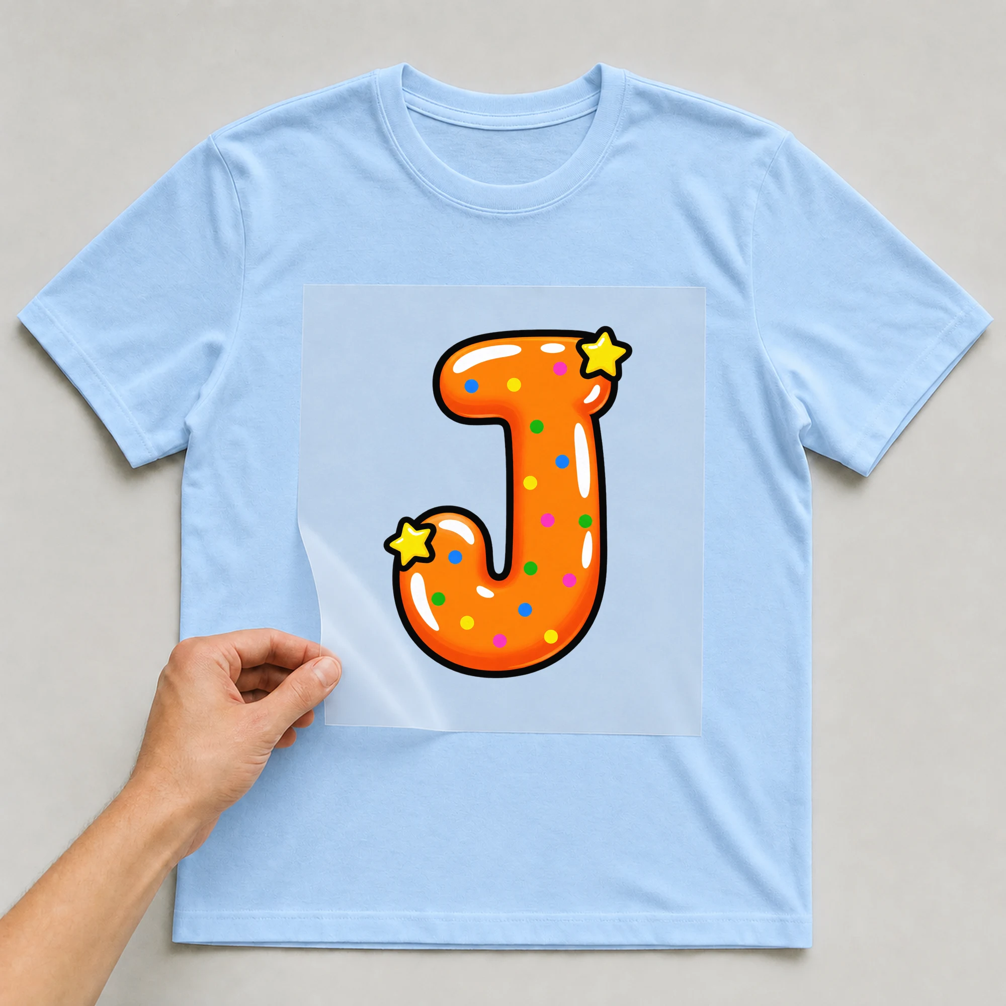 Bügelbild „Buchstabe J im Comic-Ballon-Stil“ auf babyblauem T-Shirt, Folie wird aufgelegt