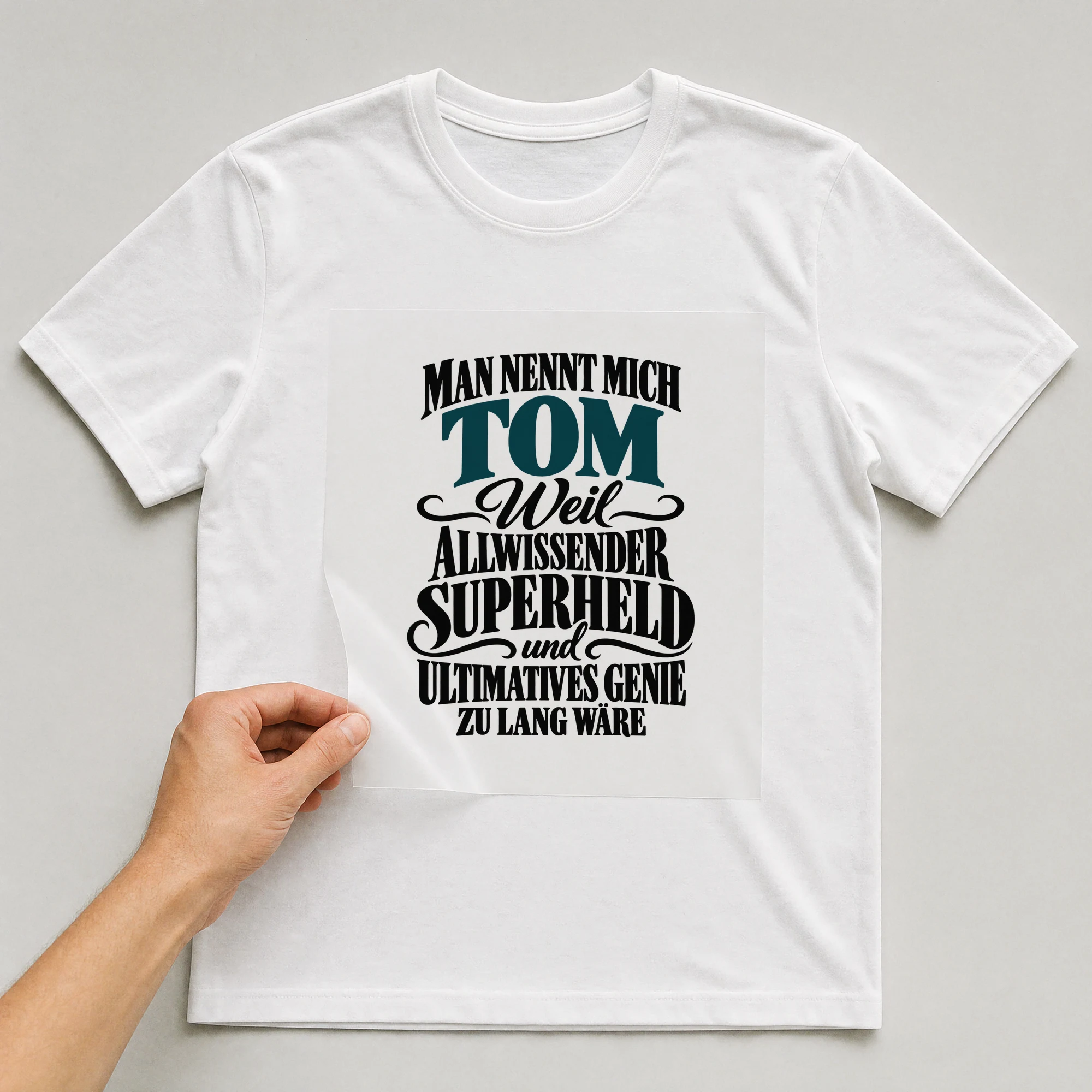 Bügelbild „Man nennt mich Tom weil allwissender Superheld und ultimatives Genie zu lang“ auf weißem T-Shirt, Folie wird aufgelegt
