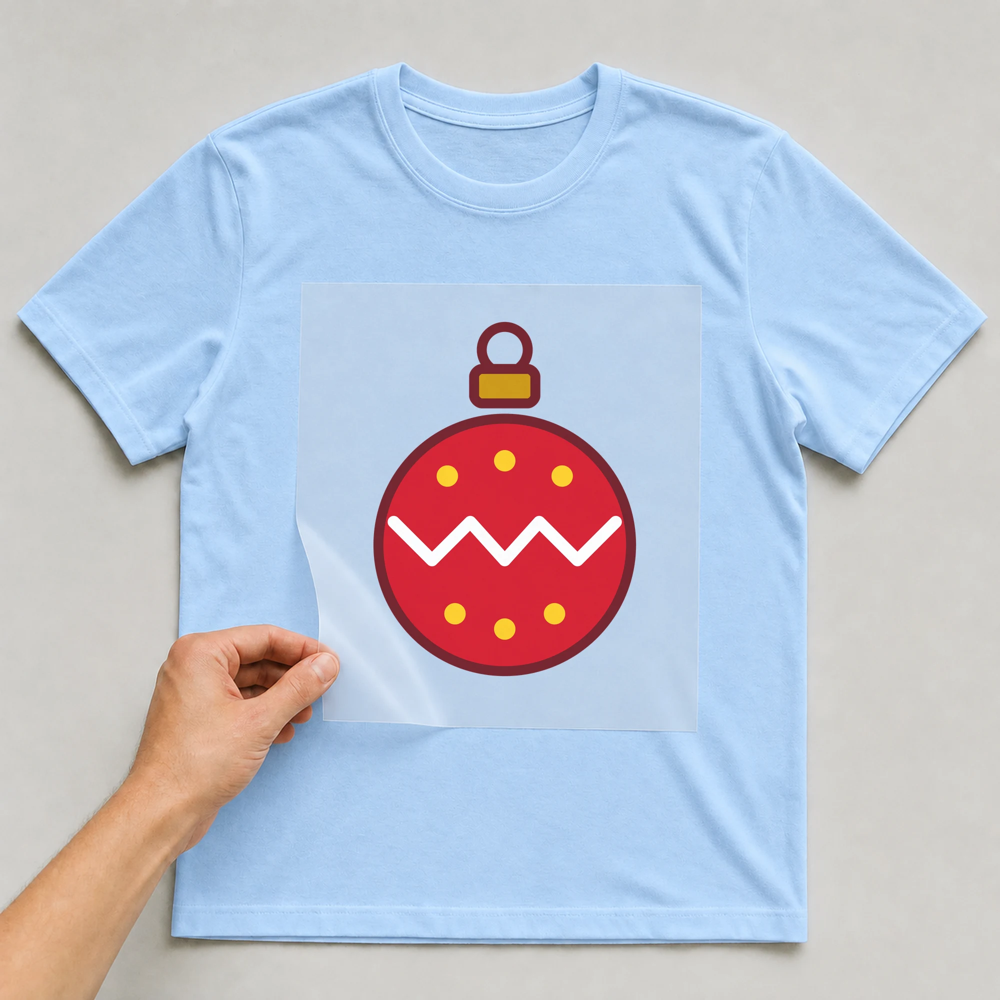 Bügelbild „Christbaumkugel“ auf babyblauem T-Shirt, Folie wird aufgelegt
