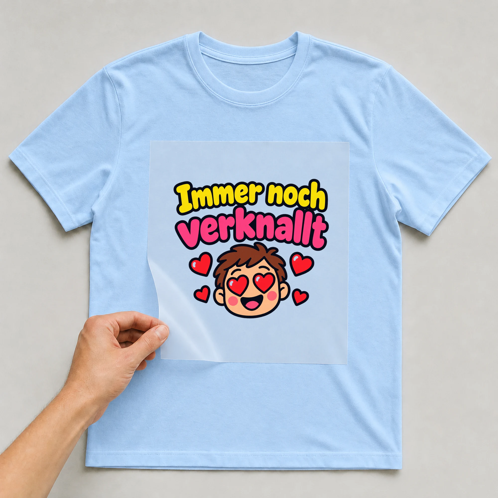 Bügelbild „Immer noch verknallt“ auf babyblauem T-Shirt, Folie wird aufgelegt
