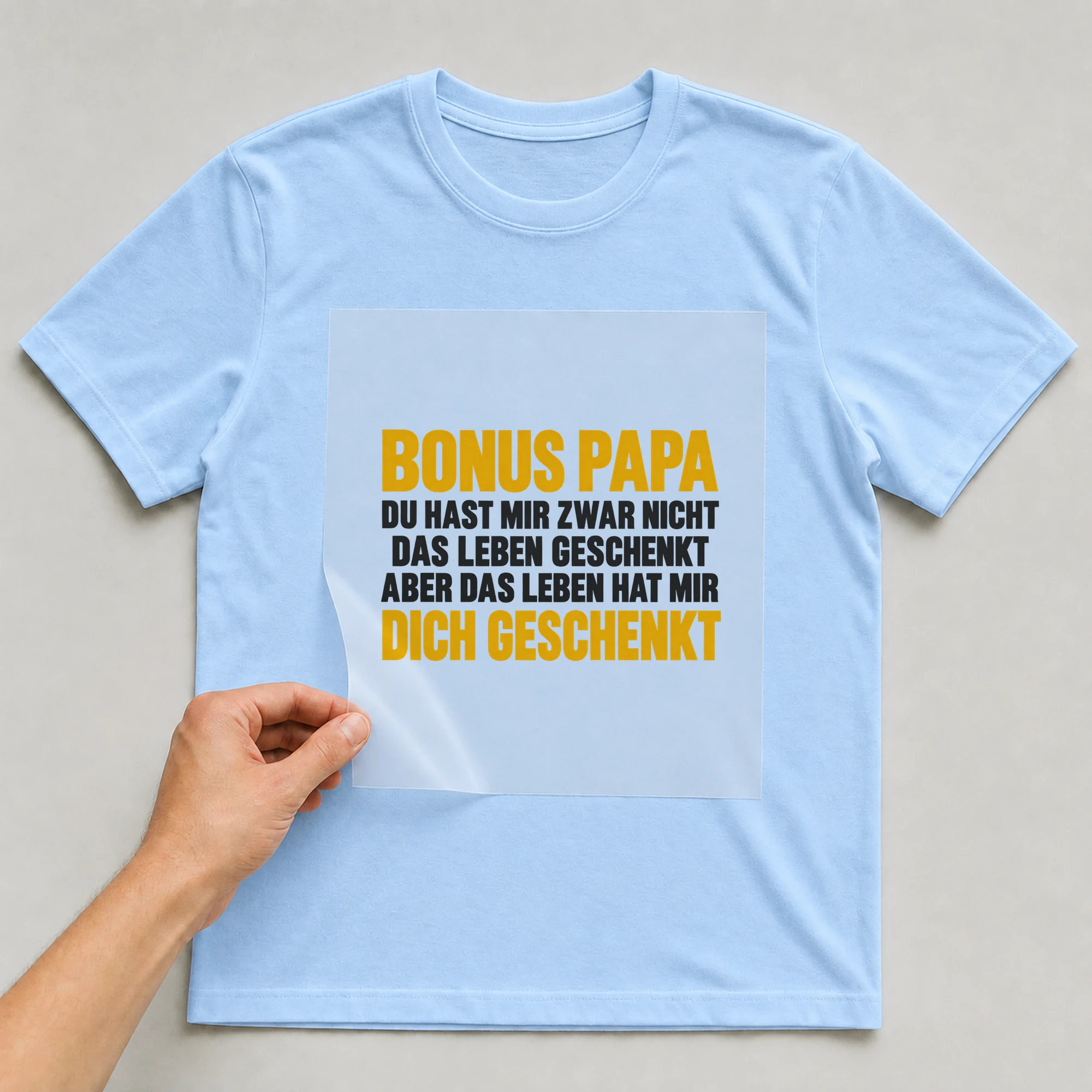 Bügelbild „Bonus Papa du hast mir zwar nicht das Leben geschenkt aber das Leben hat mir“ auf babyblauem T-Shirt, Folie wird aufgelegt