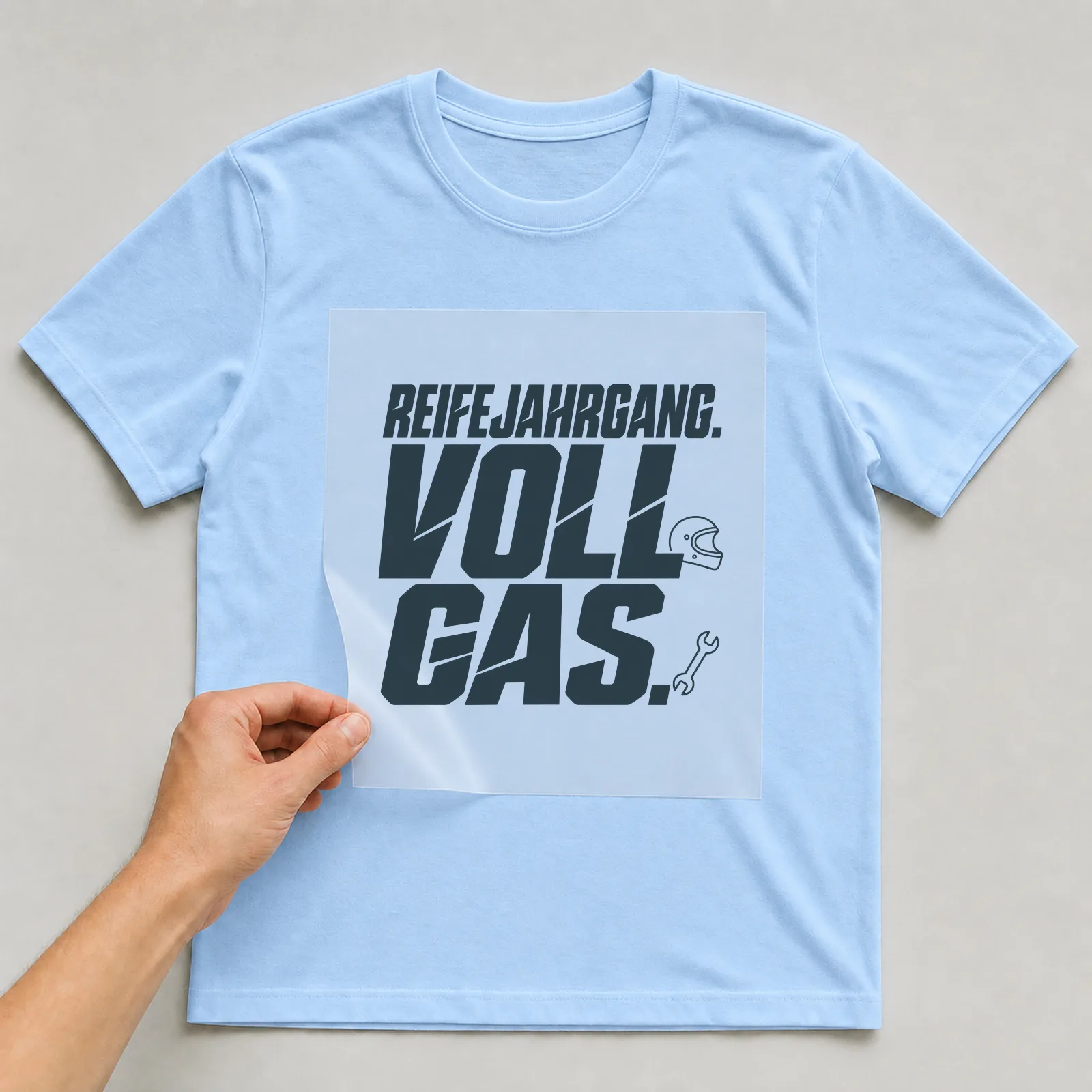 Bügelbild „Reifejahrgang. Vollgas.“ (Schrift Konturen) auf hellblauem T-Shirt, Folie wird aufgelegt