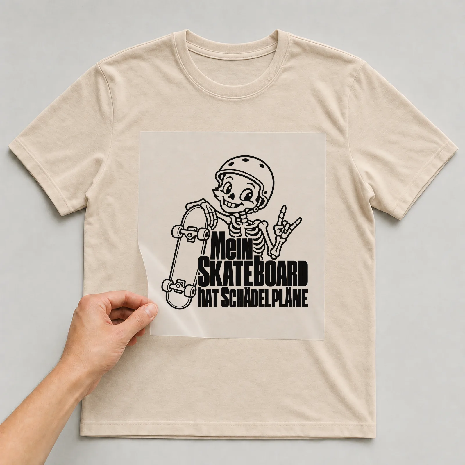 Bügelbild „Mein Skateboard hat Schädelpläne“ auf beigem T-Shirt, Folie wird aufgelegt