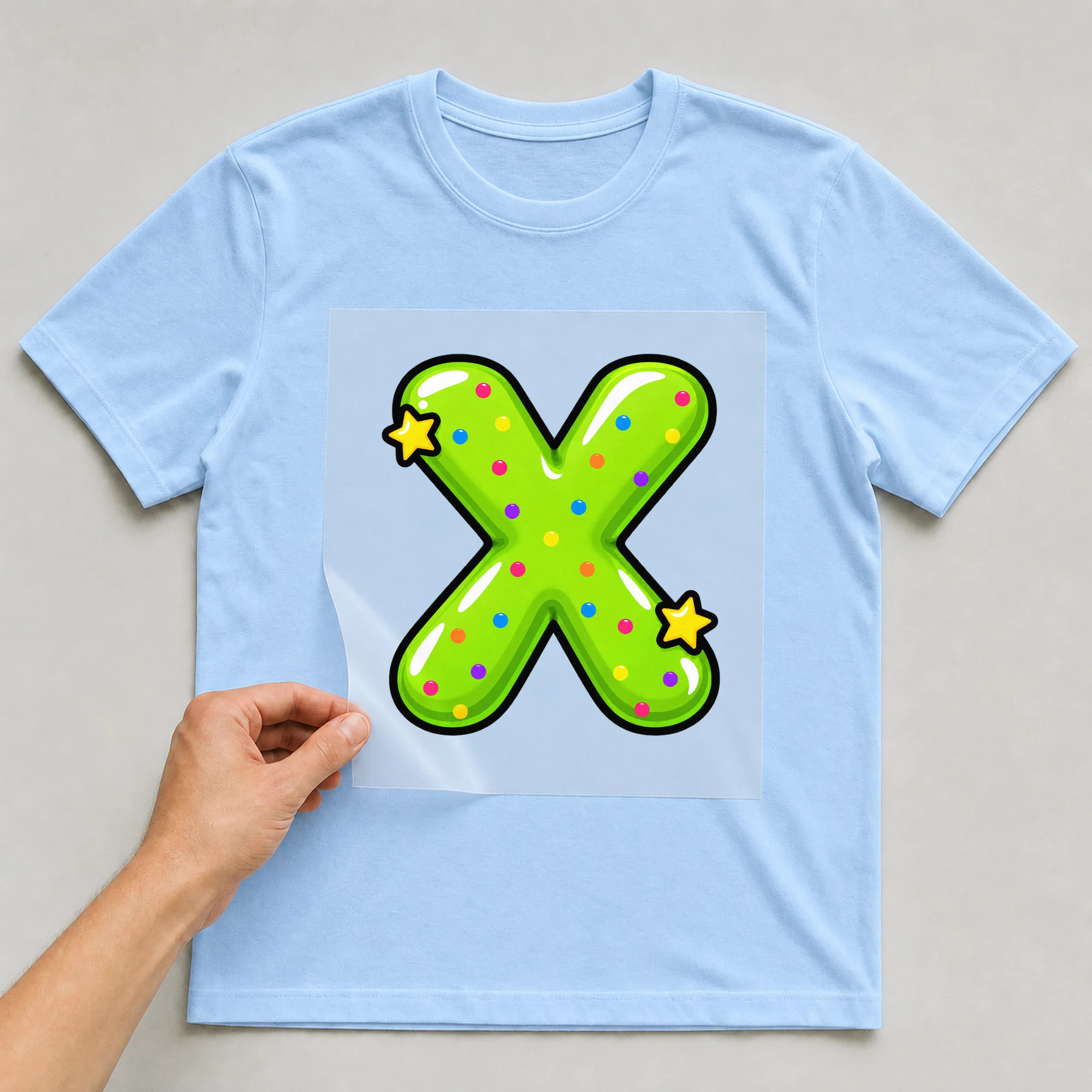 Bügelbild „Buchstabe X im Comic-Ballon-Stil“ auf babyblauem T-Shirt, Folie wird aufgelegt