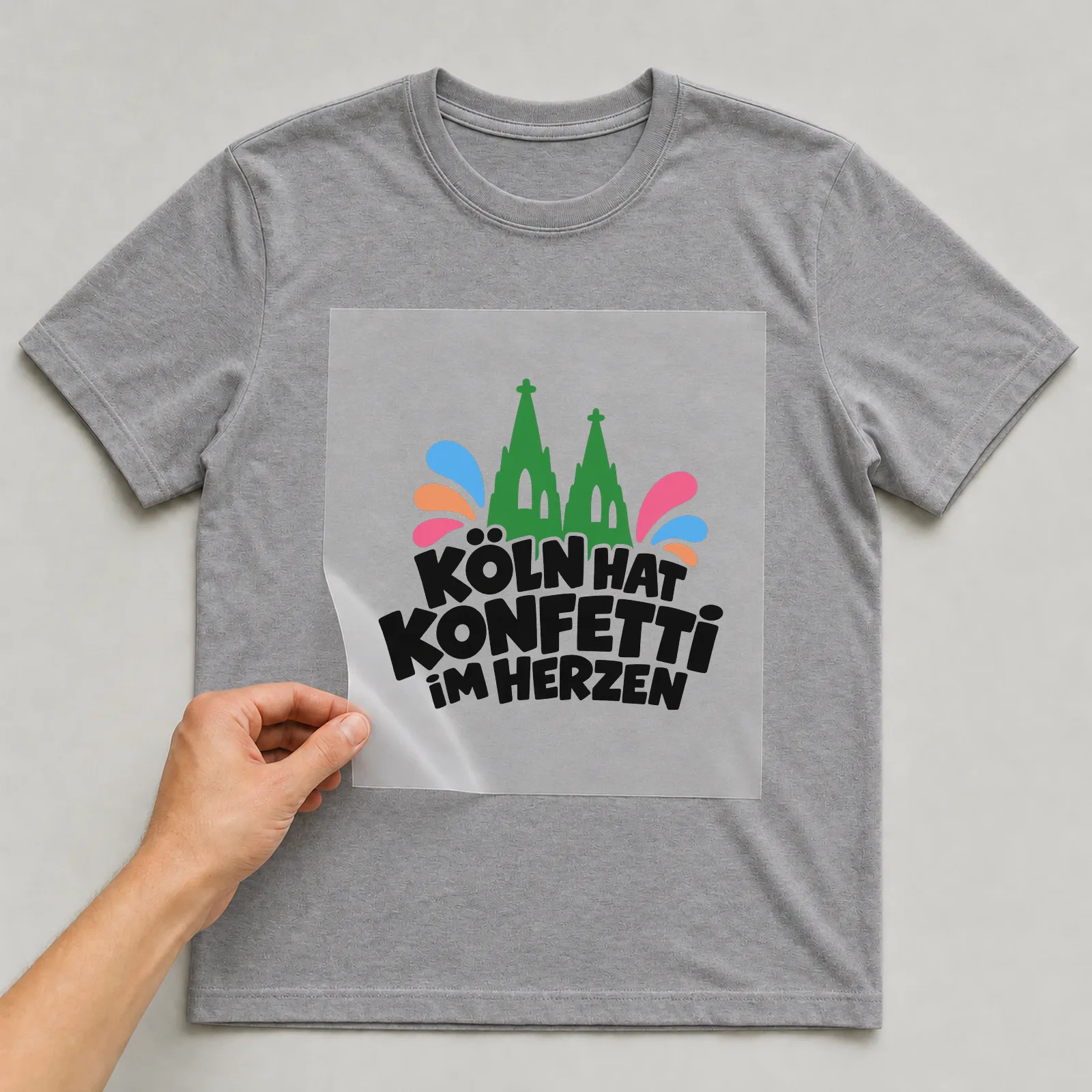 Bügelbild „Köln hat Konfetti im Herzen“ auf grauem T-Shirt, Folie wird aufgelegt
