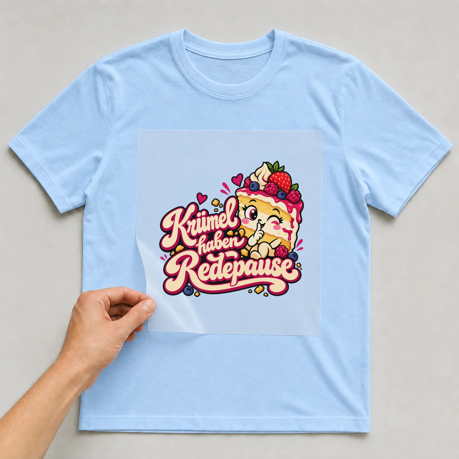 Bügelbild „Krümel haben Redepause“ auf hellblauem T-Shirt, Folie wird aufgelegt