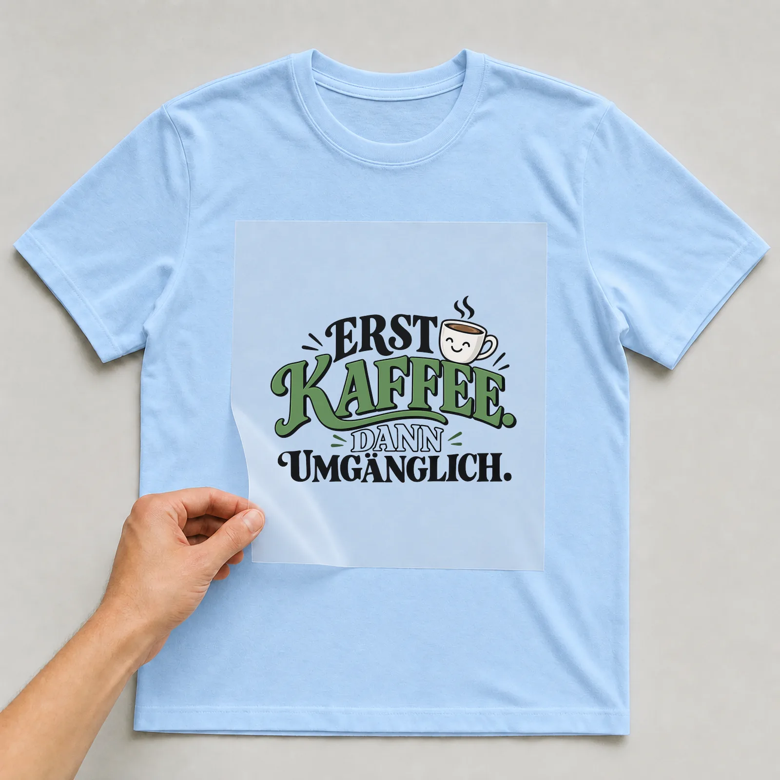 Bügelbild „Erst Kaffee. Dann umgänglich.“ auf hellblauem T-Shirt, Folie wird aufgelegt