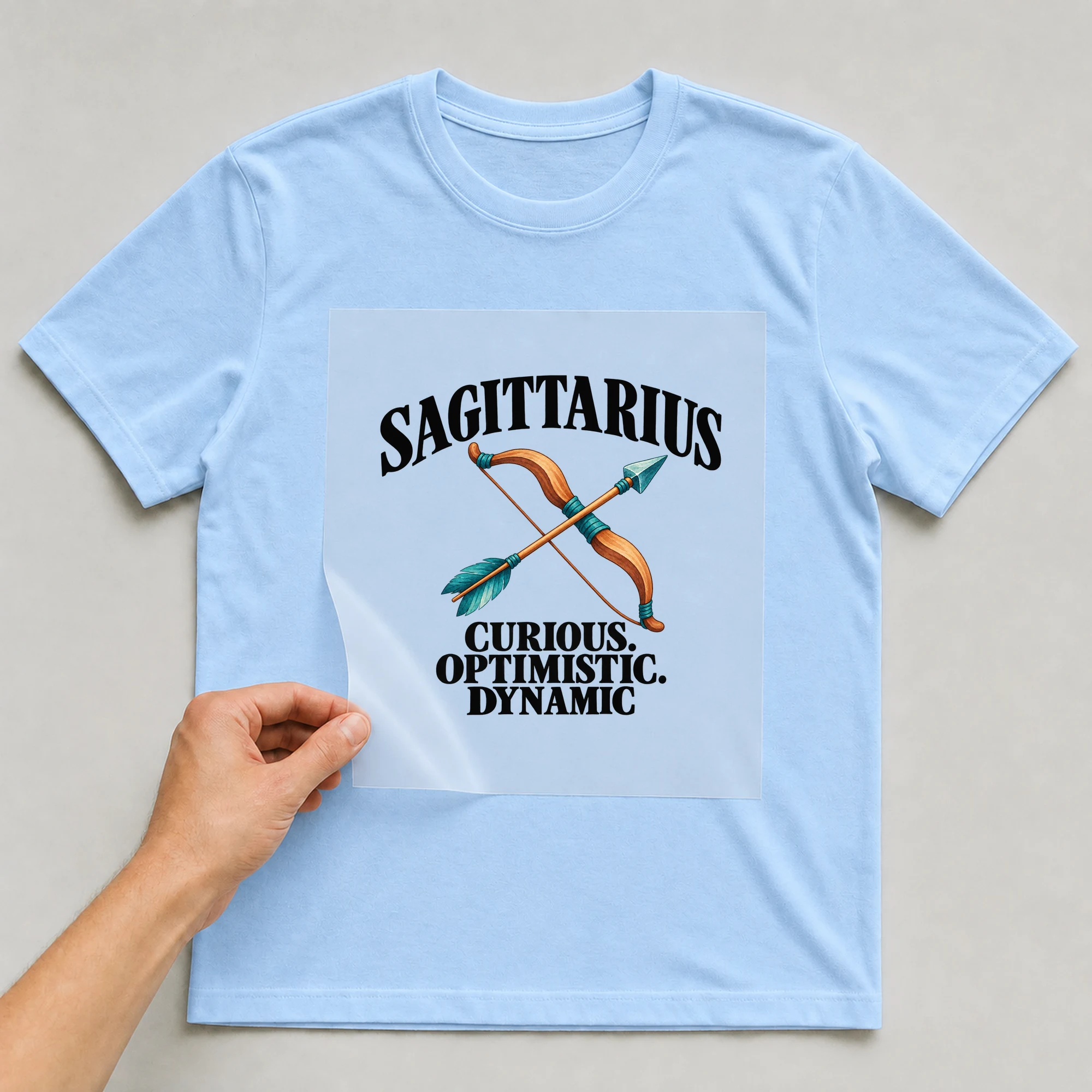 Bügelbild „Sagittarius Curious. Optimistic. Dynamic“ auf babyblauem T-Shirt, Folie wird aufgelegt