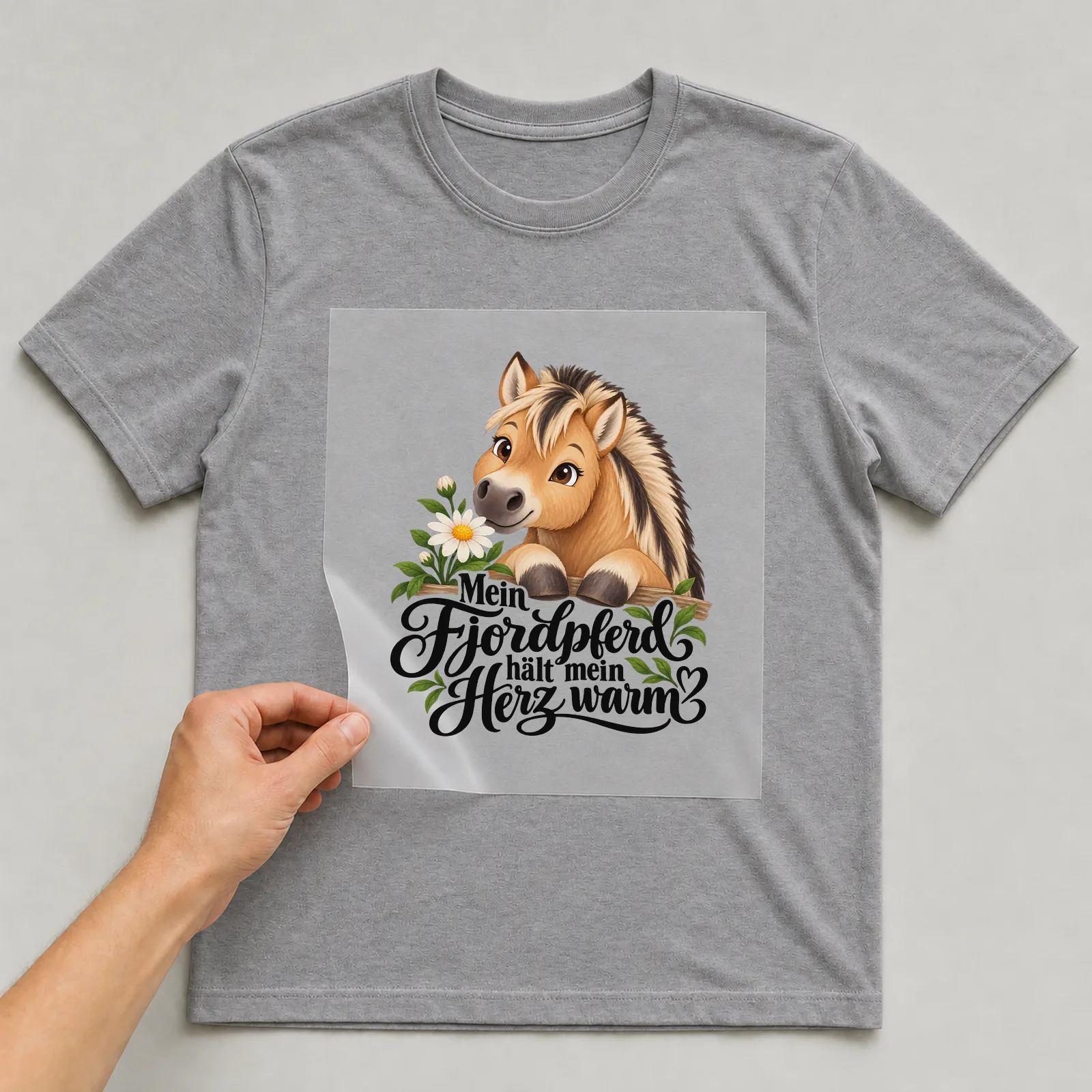 Bügelbild „Mein Fjordpferd hält mein Herz warm“ auf grauem T-Shirt, Folie wird aufgelegt