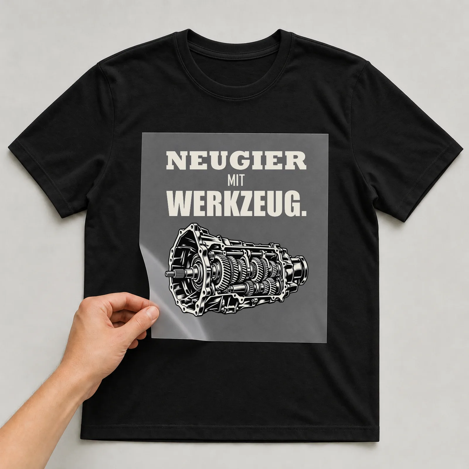 Bügelbild „Neugier mit Werkzeug“ auf schwarzem T-Shirt, Folie wird aufgelegt