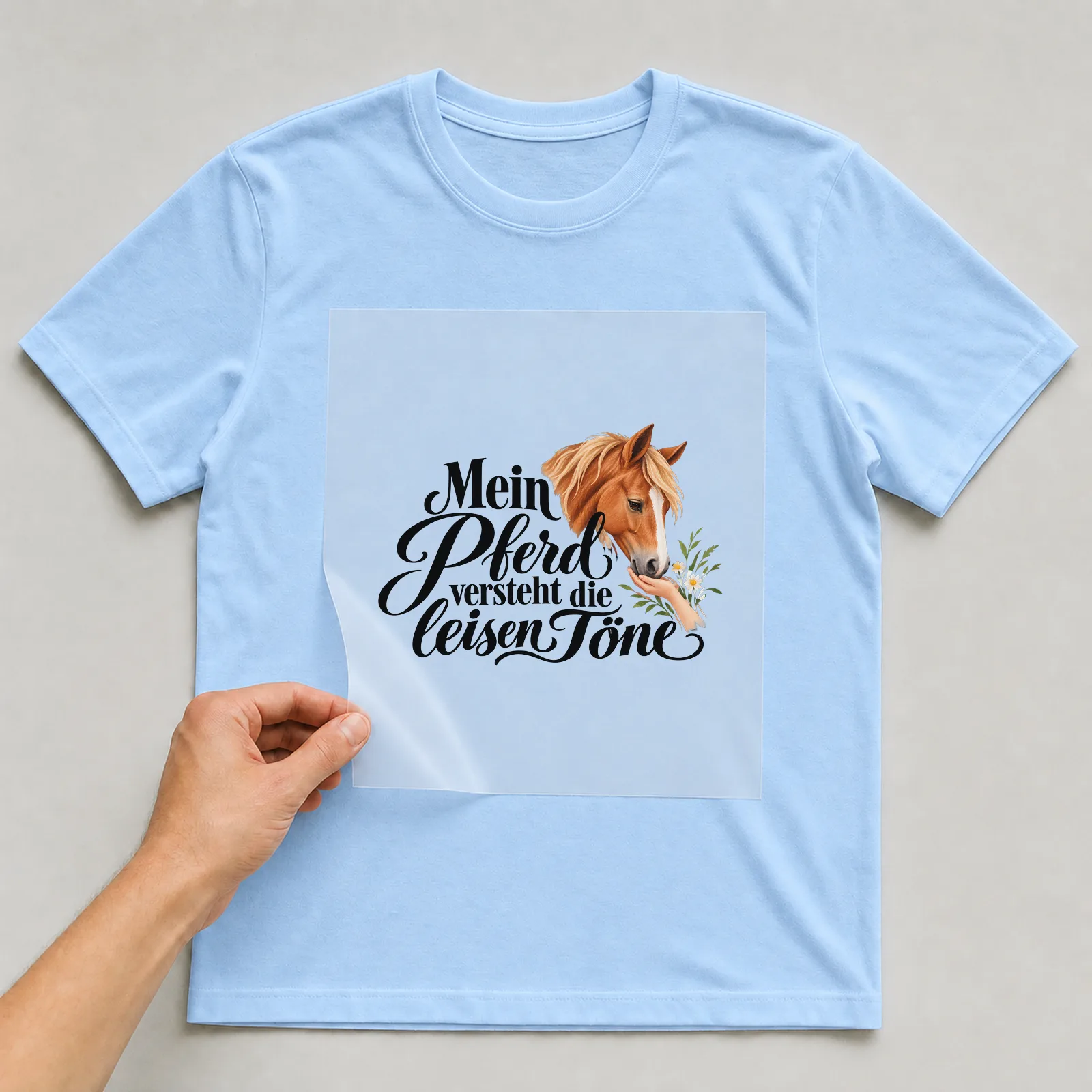 Bügelbild „Mein Pferd versteht die leisen Töne“ auf hellblauem T-Shirt, Folie wird aufgelegt